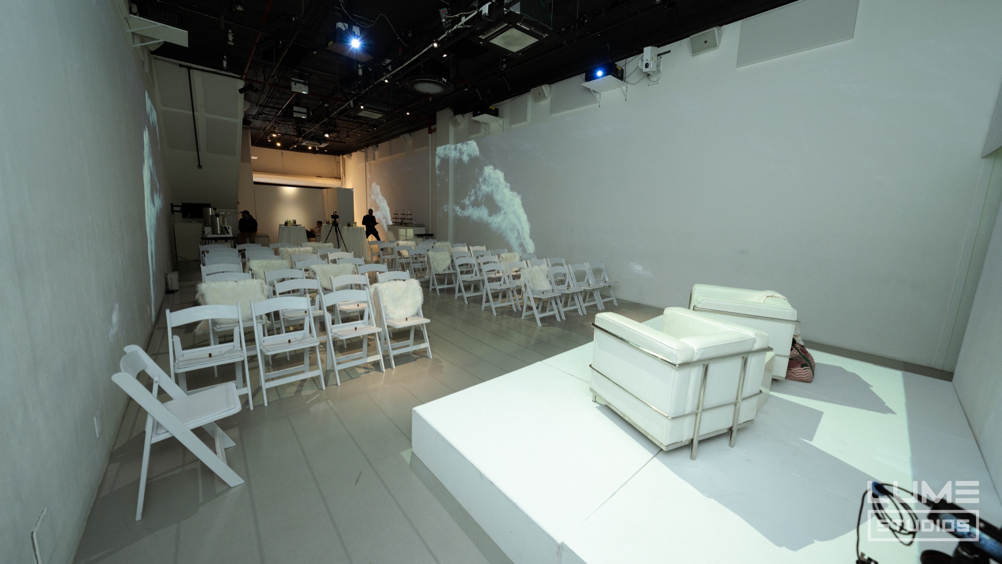 All white room with folding chairs, a white armchair on a low platform and a faint projection on the wall