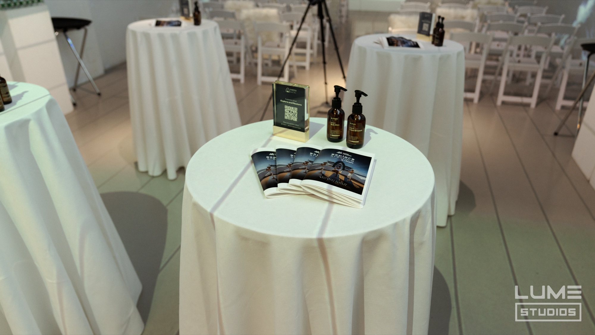 Round white draped cocktail table with two amber bottles, a QR card and fanned brochures, chairs behind