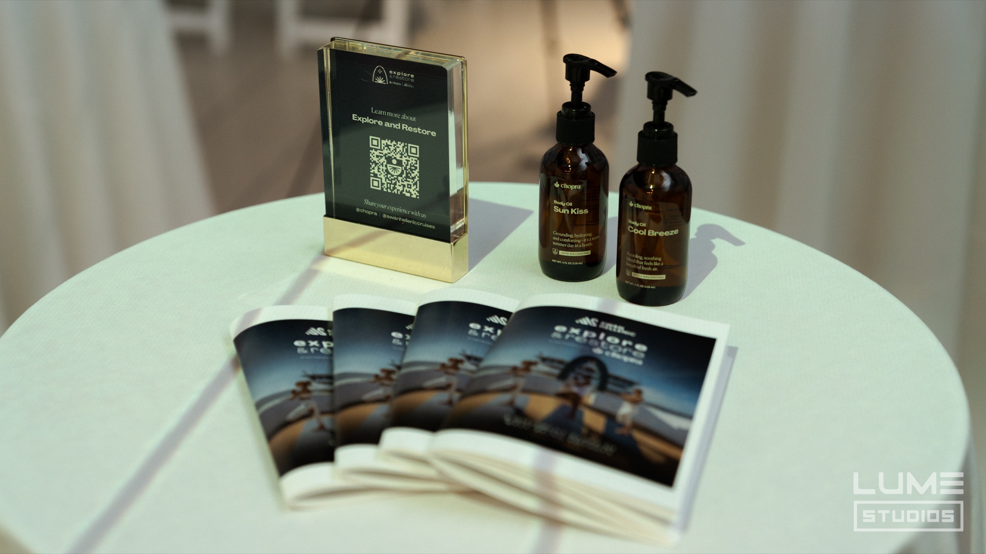 Two amber pump bottles, a framed QR card and fanned Explore and Restore pamphlets on a round white table