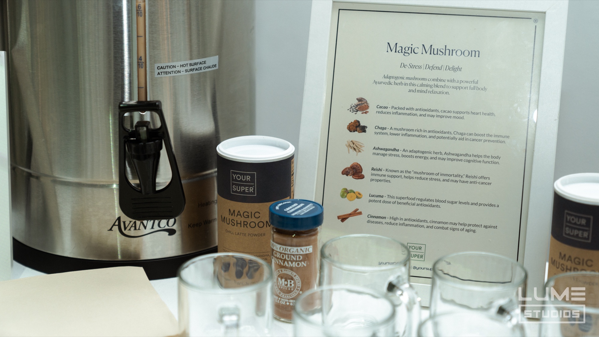 Silver coffee urn, jars of Magic Mushroom powder and glass mugs in front of a printed ingredient sign