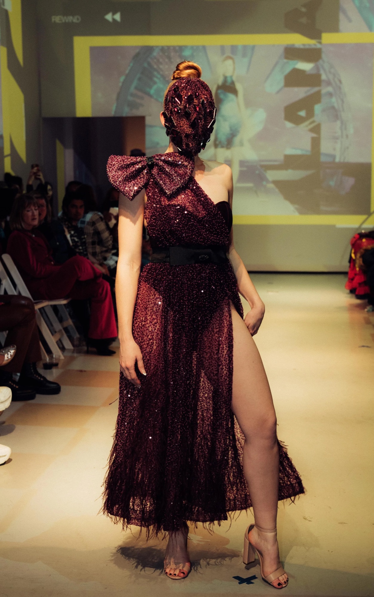 Model in a burgundy sequin gown with a shoulder bow pauses on the DigitalAX runway