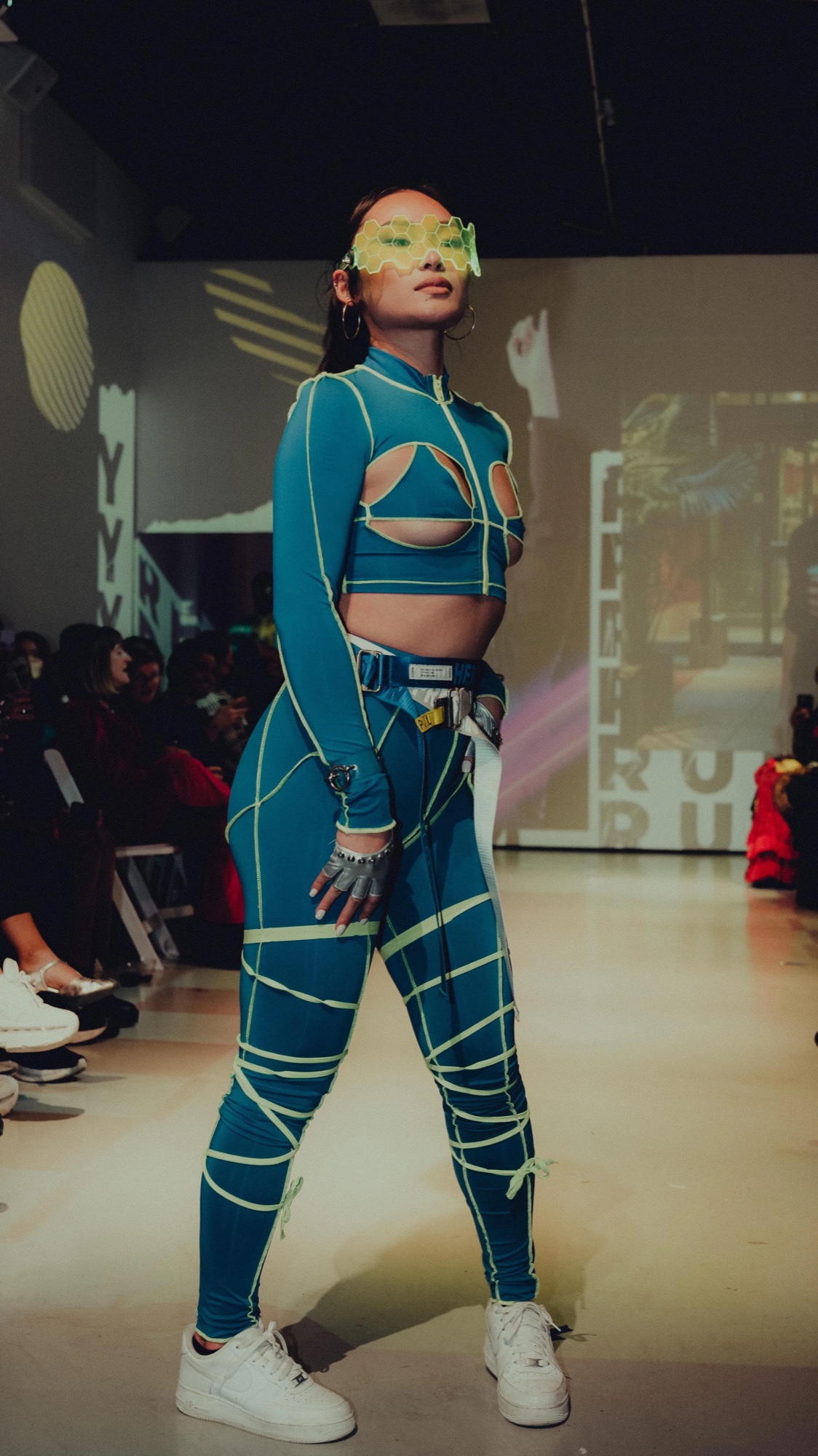 Model in a teal outfit strapped with yellow cord and a green visor on the DigitalAX runway