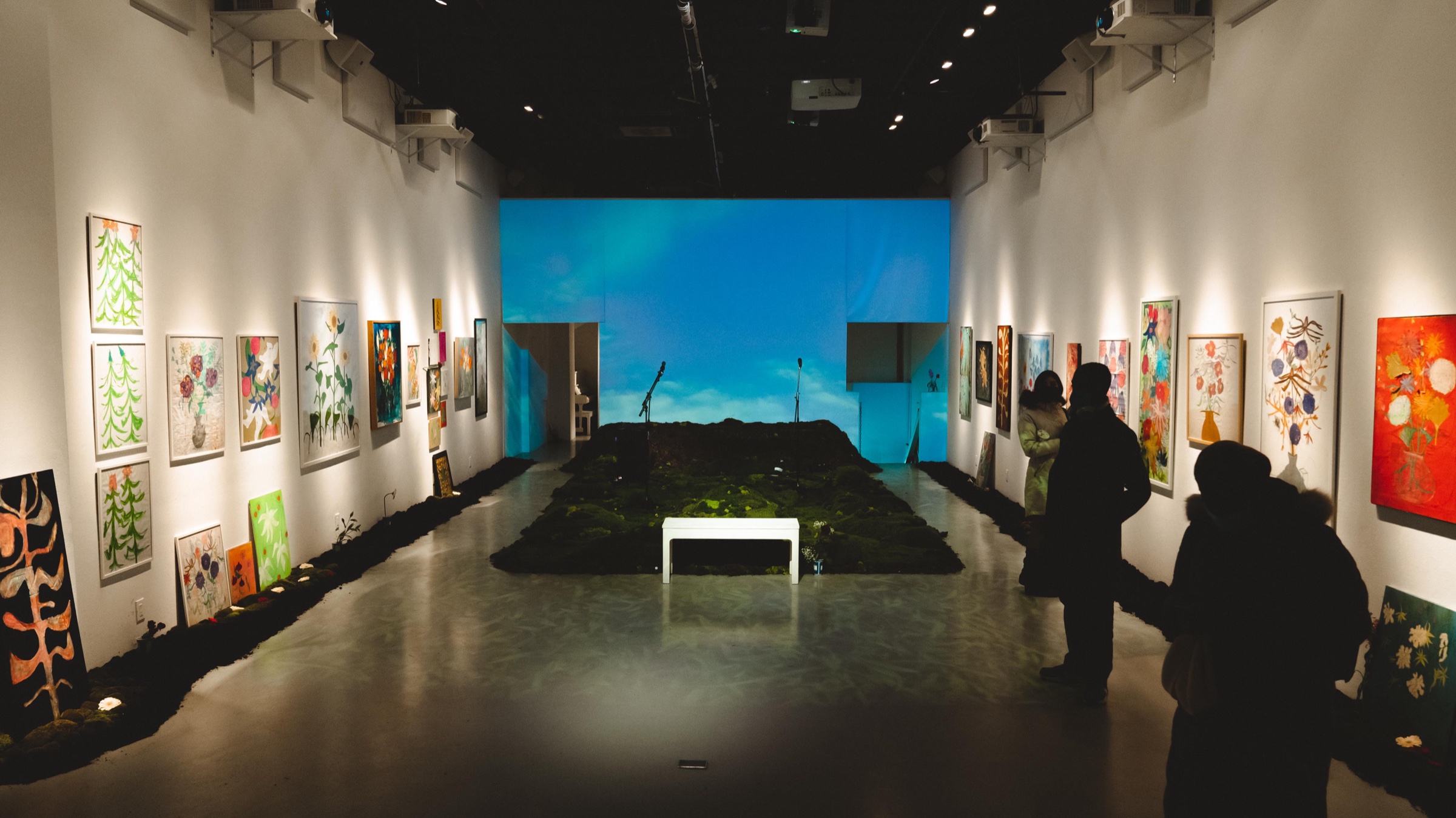 Gallery view of the Dirty Flowers show with floral paintings, a moss installation and glowing sky screen