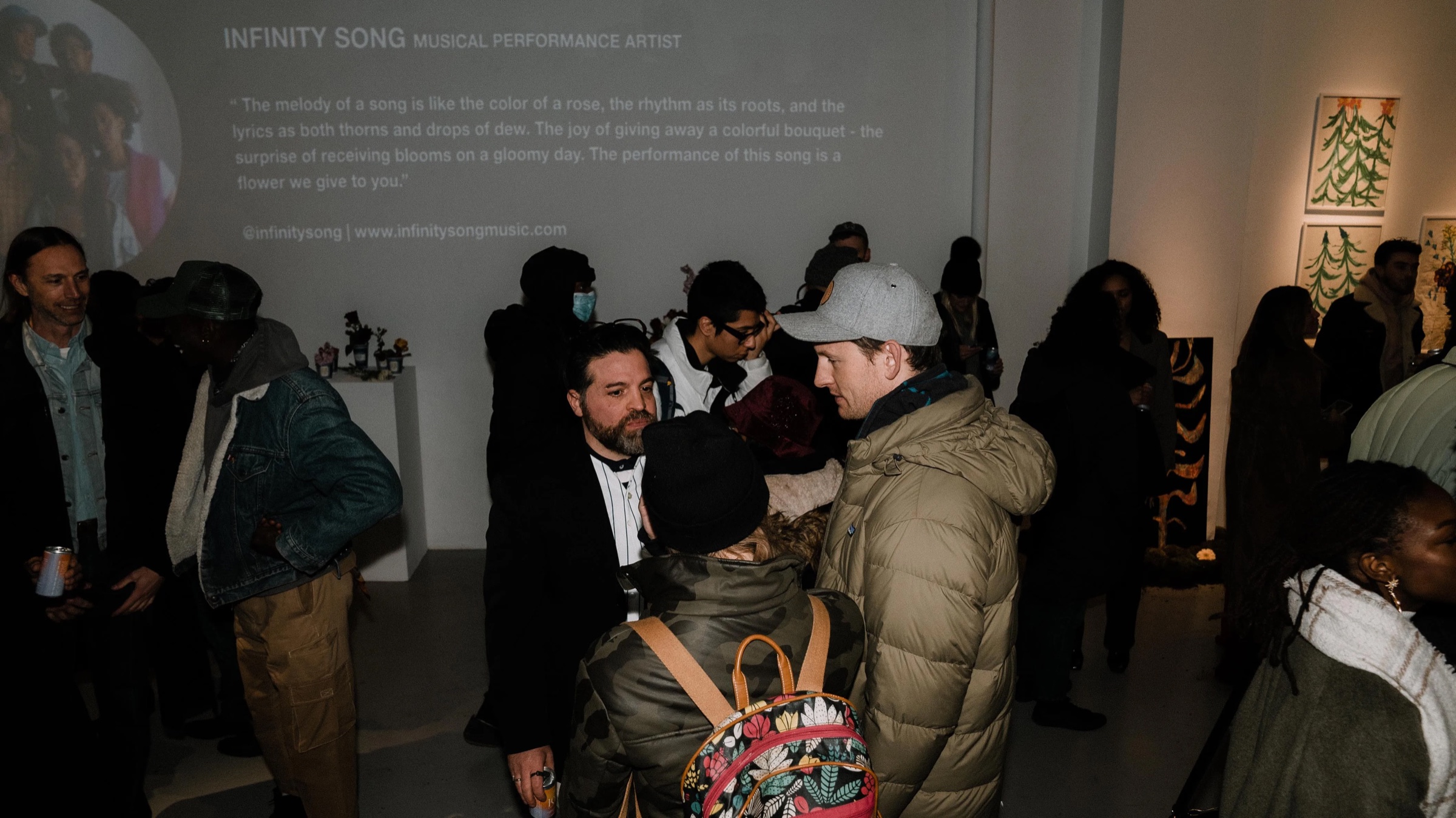 Guests mingle beneath a projected artist statement for Infinity Song at Dirty Flowers
