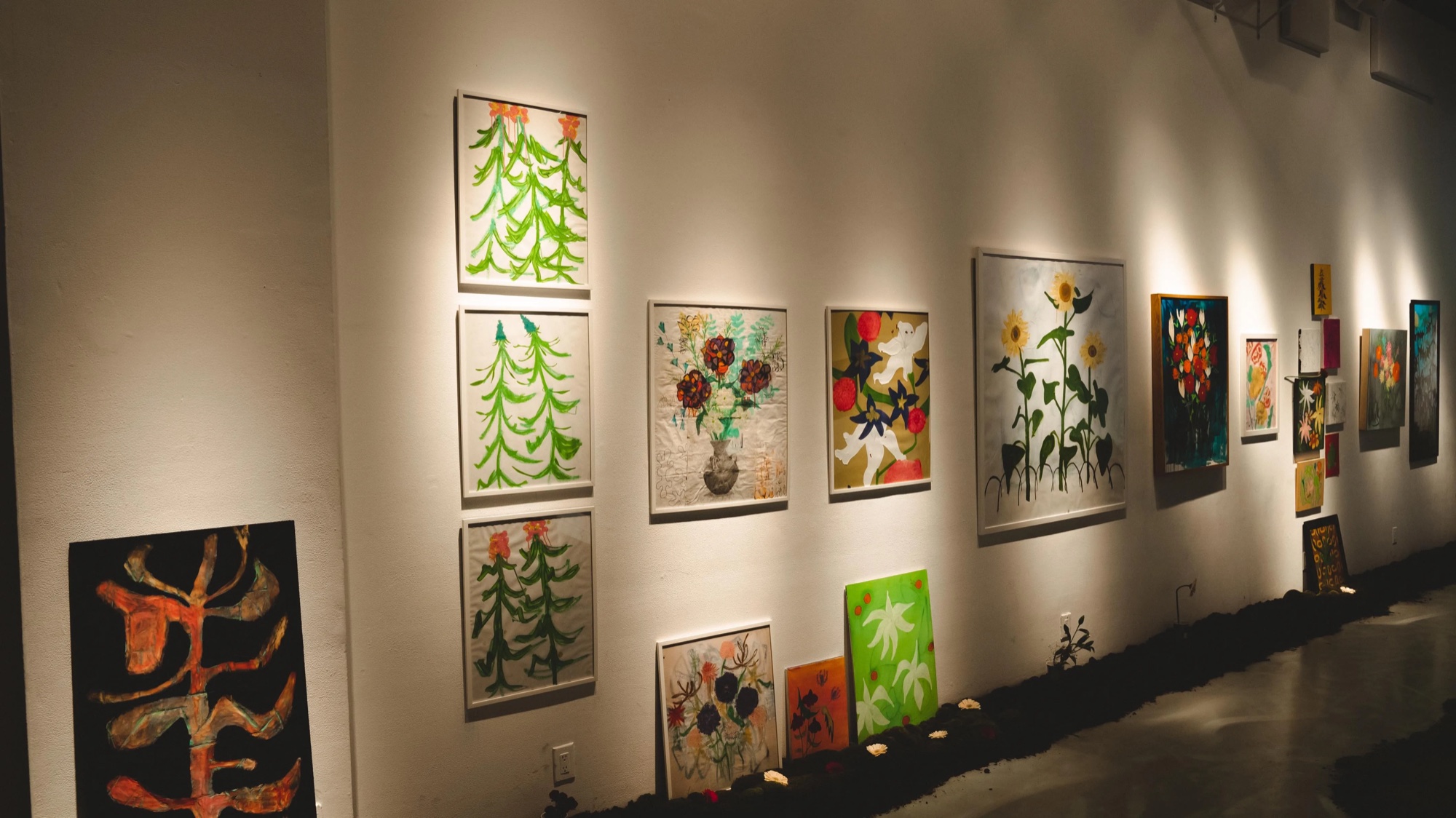 Gallery wall of flower paintings under warm spotlights at the Dirty Flowers exhibition