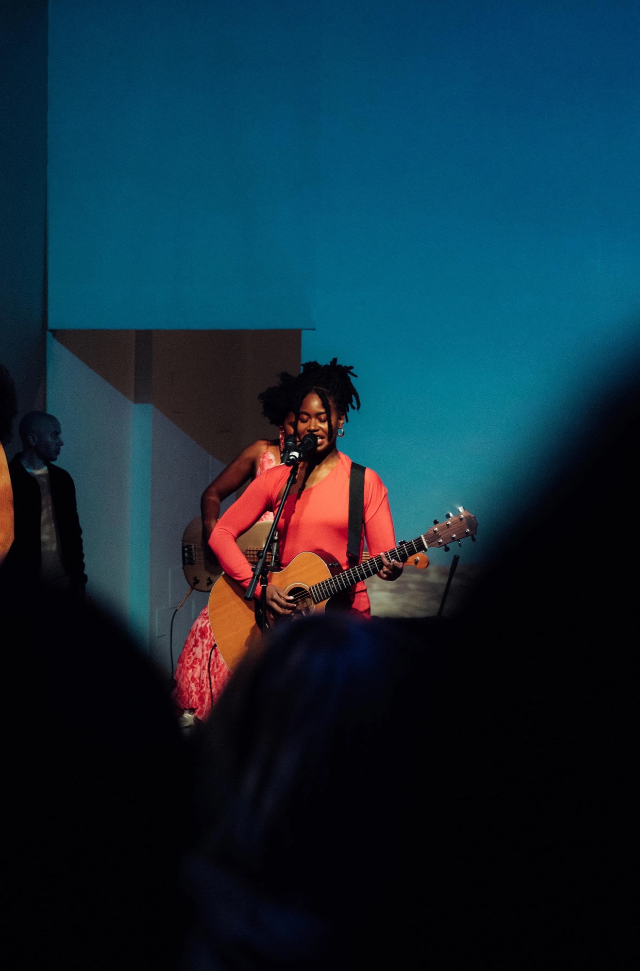 Singer in a red dress plays guitar under deep blue light at the Dirty Flowers opening