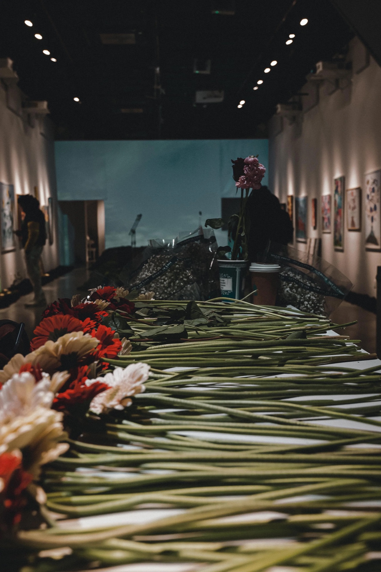 Long row of cut flowers laid along the gallery floor between the Dirty Flowers paintings