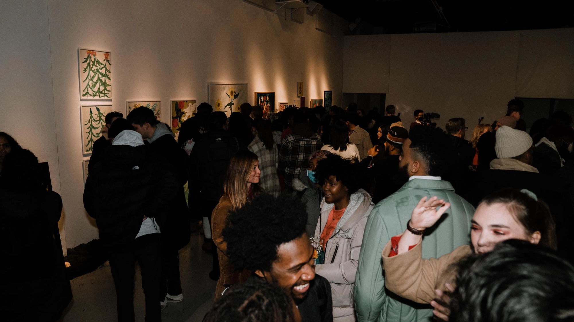 Crowd fills the Dirty Flowers gallery with paintings glowing on the walls behind them