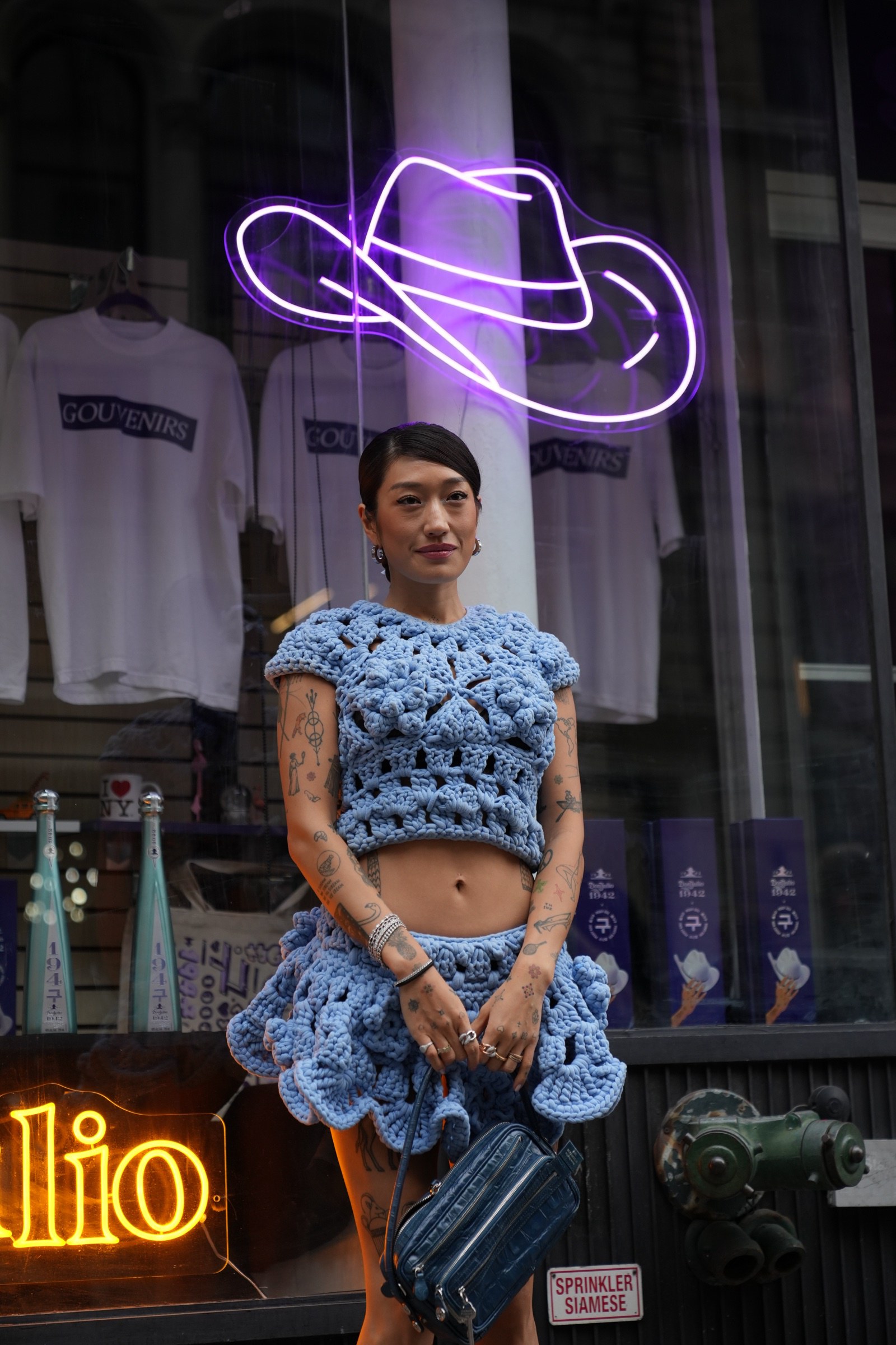 Sideways view of a person in blue crochet beside a purple neon figure and Don Julio signage in a window