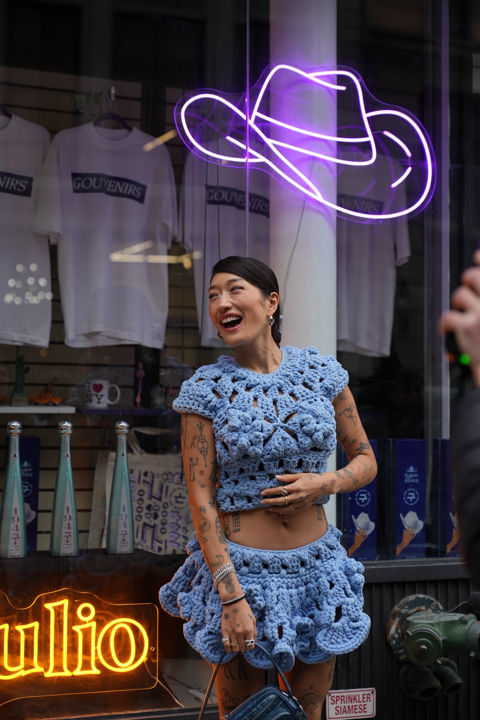 A woman in a blue crochet dress laughs beside a purple neon cowboy hat under an orange Don Julio sign