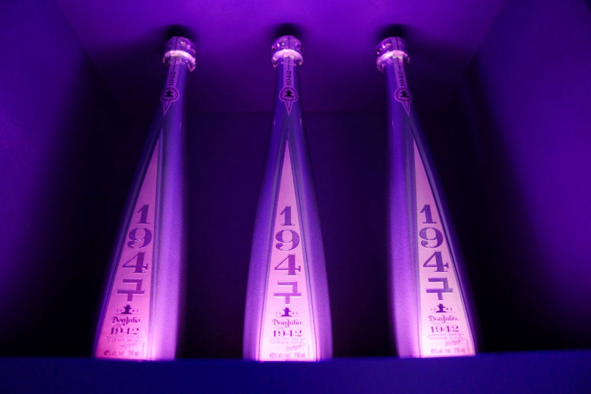 Three Don Julio 1942 bottles marked 1947 glow inside a display niche under purple lighting