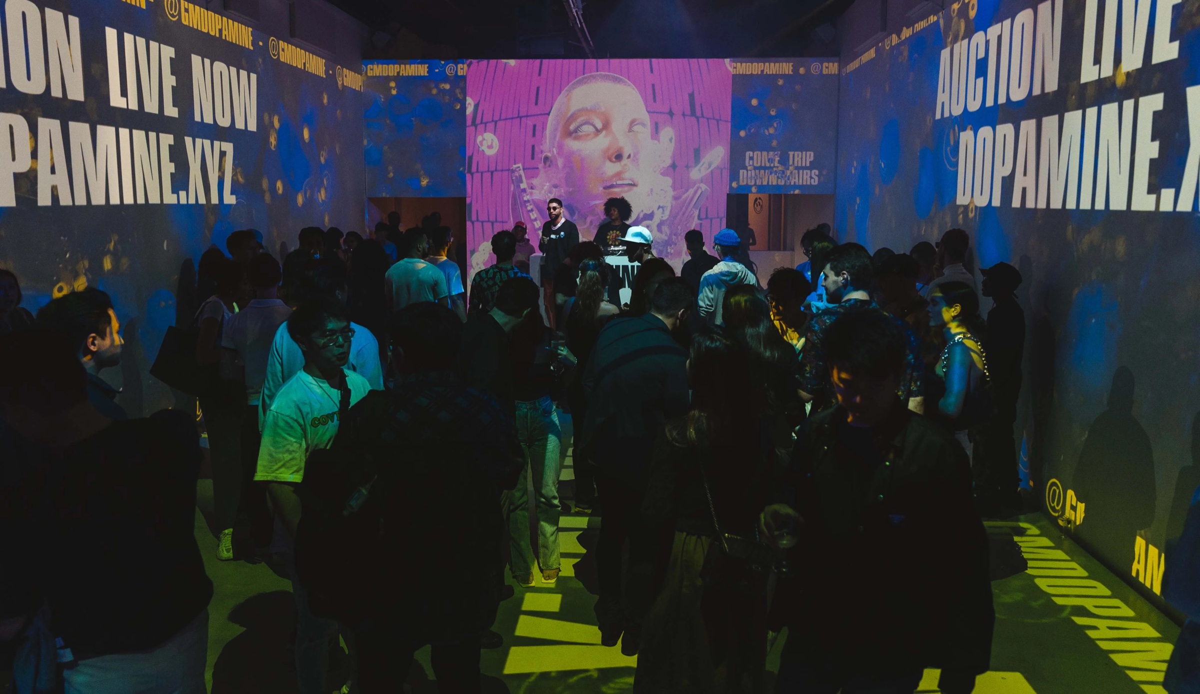 Crowd gathers beneath projected walls announcing the live Dopamine auction