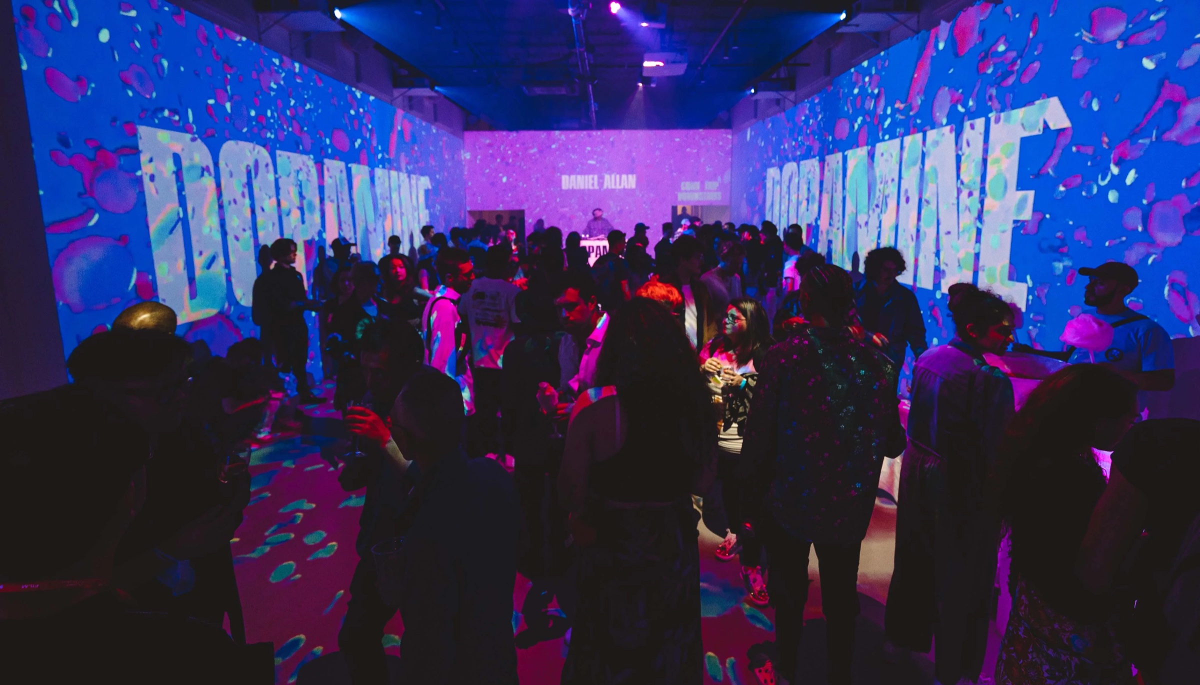 Crowd beneath a blue Dopamine projection splashed with pink paint at Lume Studios