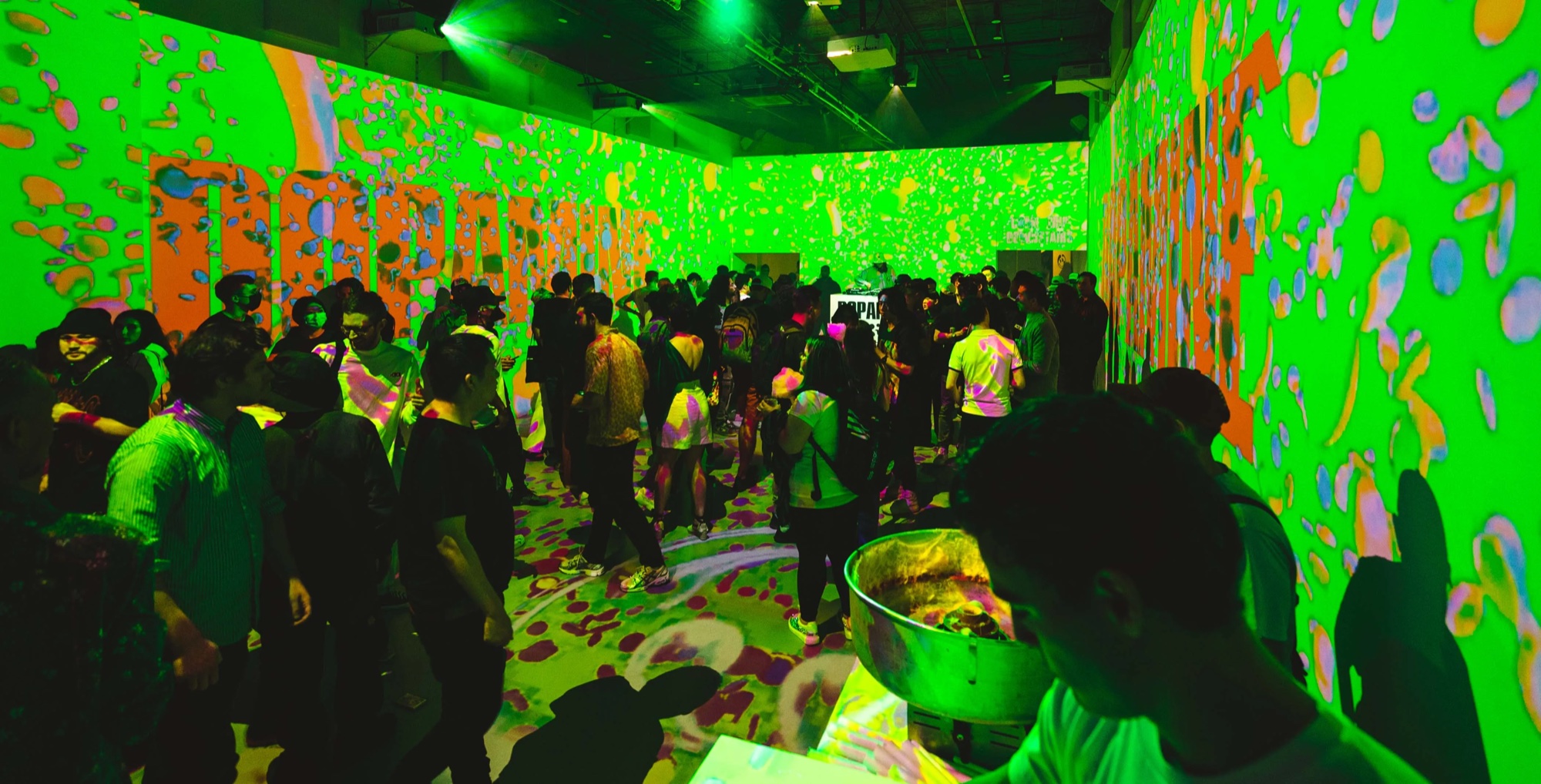 Guests walk through a room drenched in green and orange splatter projections at Dopamine