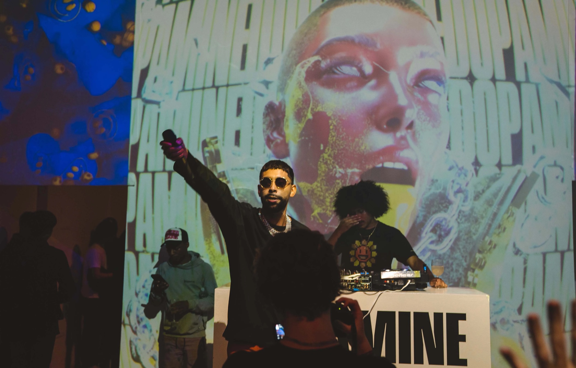 DJ points to the crowd in front of a giant projected face at the Dopamine party