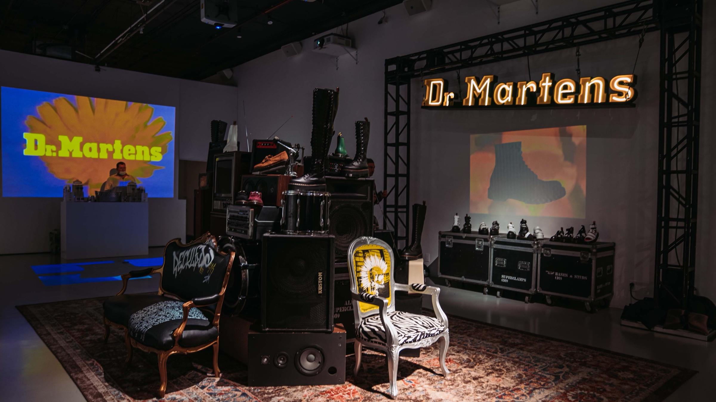 Dr. Martens showcase with a glowing marquee sign, stacked speakers topped with boots and eclectic vintage chairs