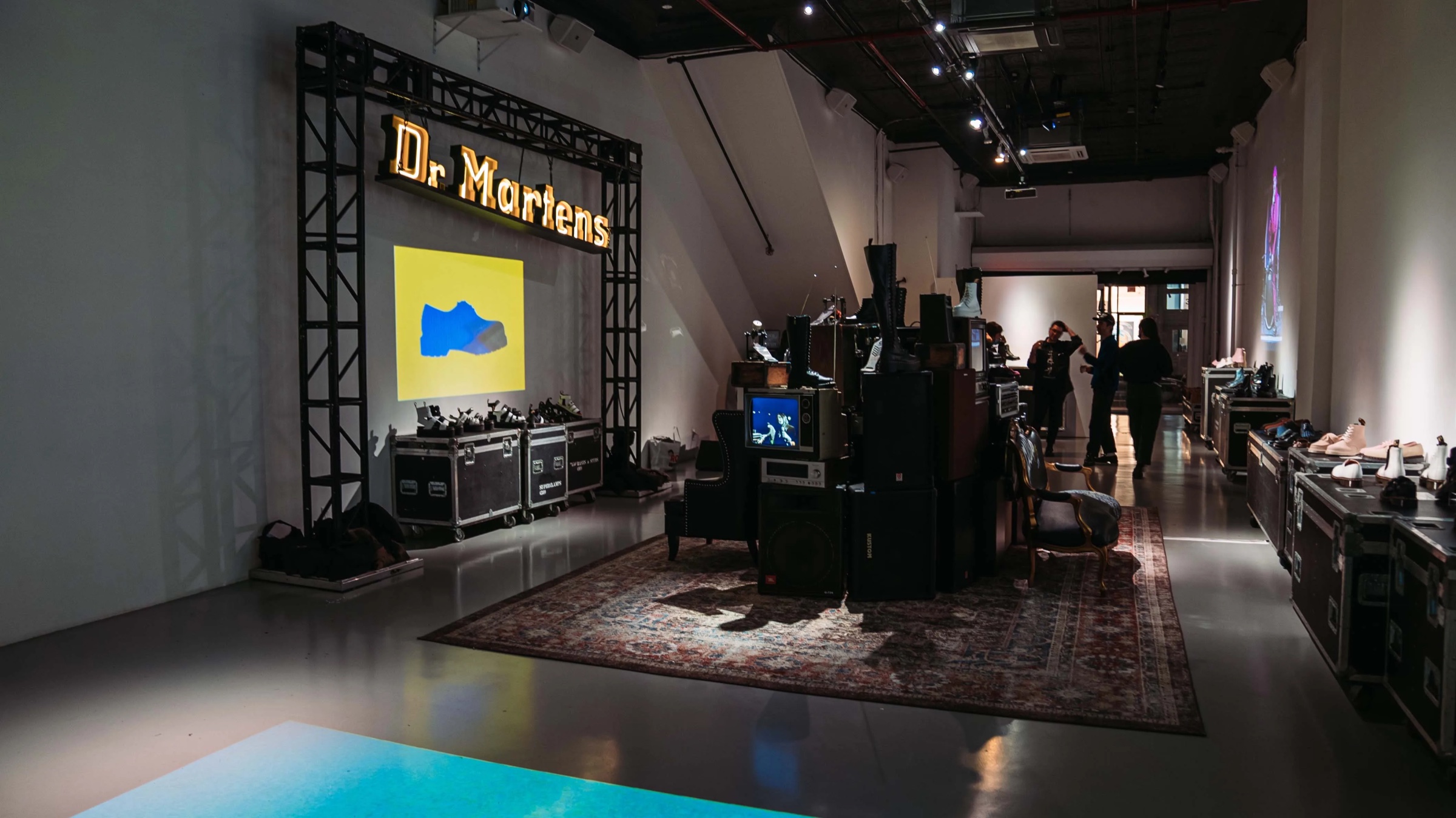 Dr. Martens marquee sign on a truss above a projected yellow boot in a rug lined room
