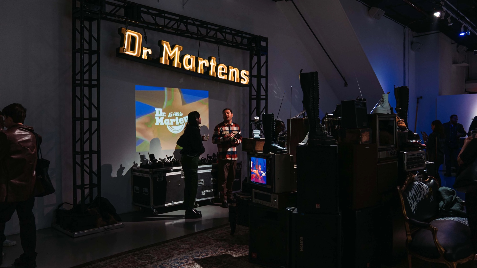 Guests browse boots on road cases beneath the Dr. Martens sign in blue and orange light