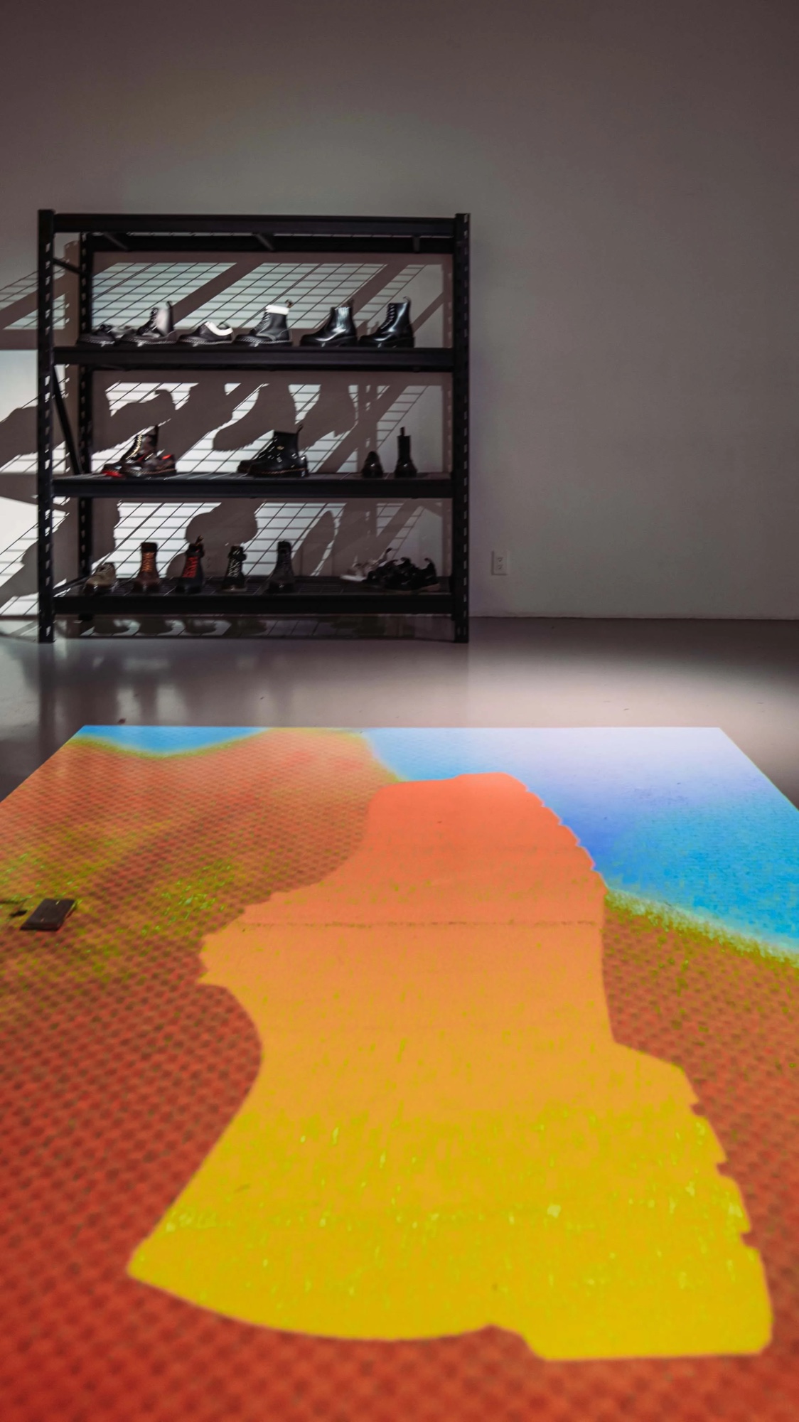 Shelf of Dr. Martens boots above a floor projection of an orange boot silhouette