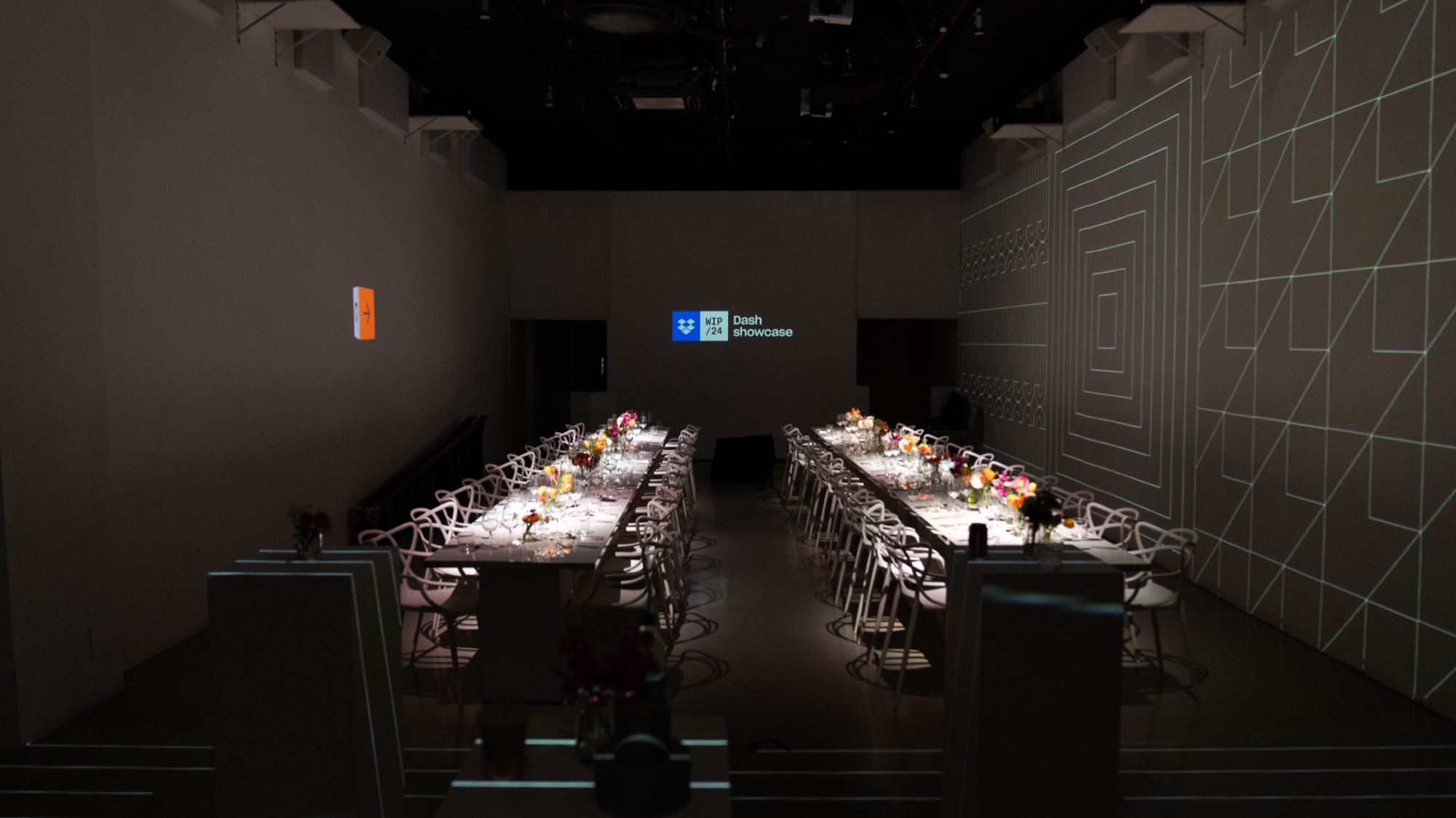 Dim hall with two long dinner tables lit by candles beneath a small blue Dash showcase projection