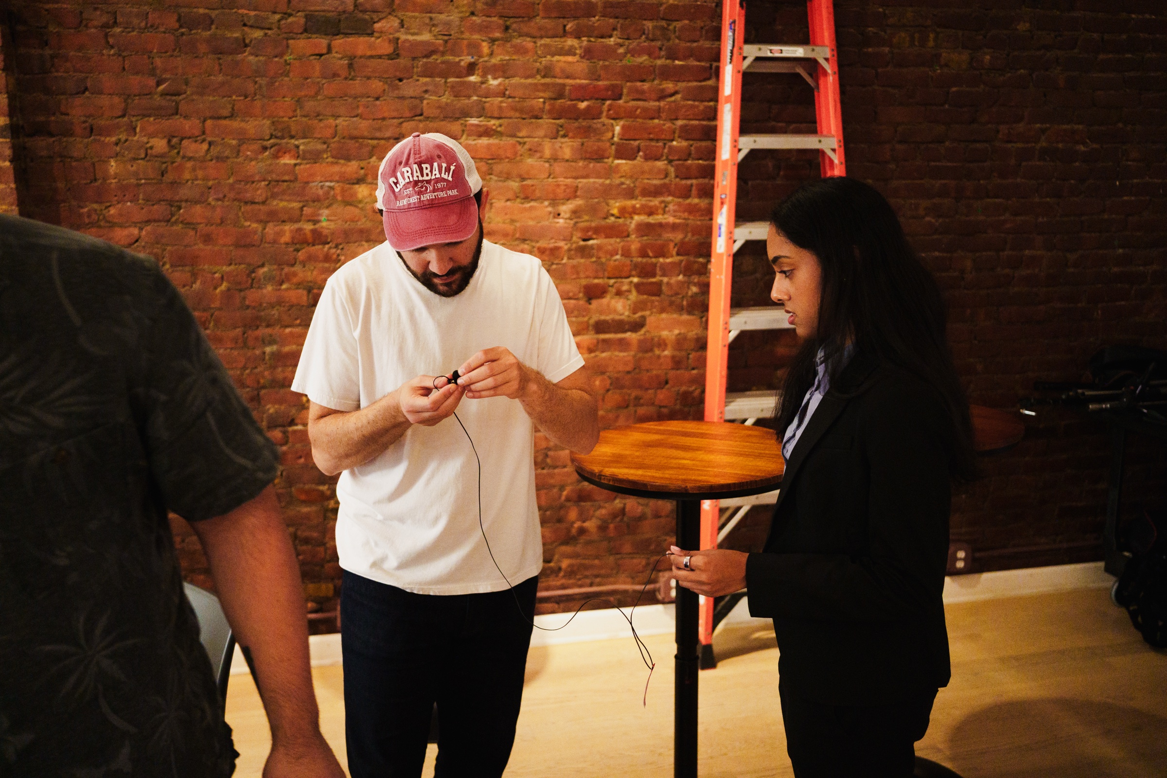 Doctor Mike in a pink cap untangles a lapel microphone cable while a woman watches beside him