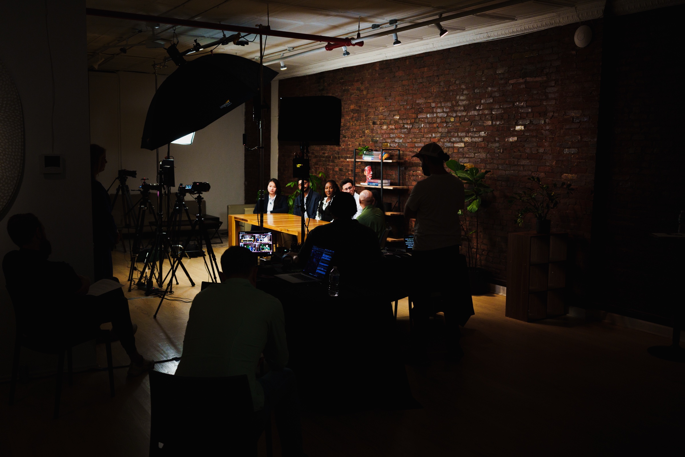 Wide dark view of the studio, the lit table at the far end with crew watching monitors