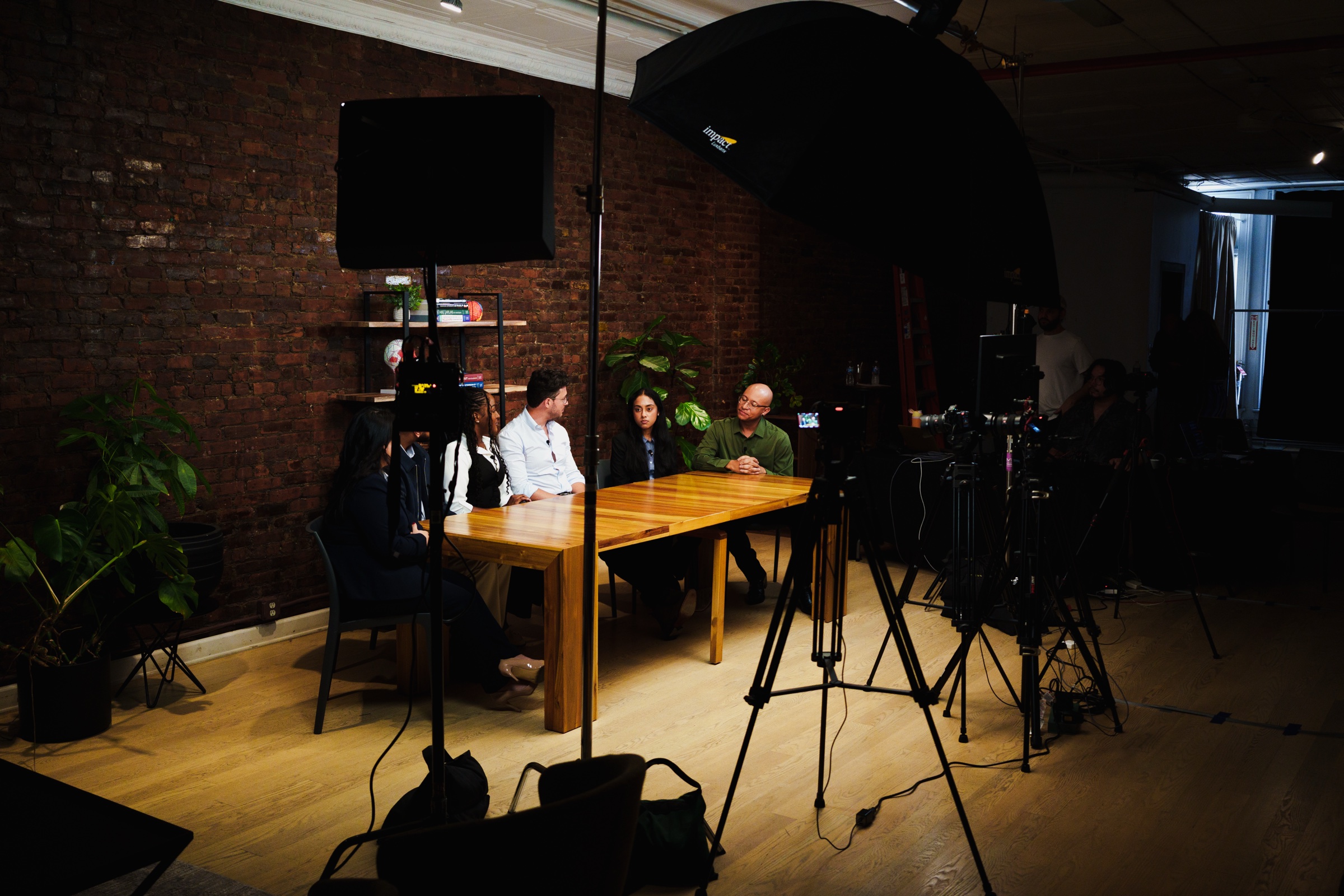 Two guests and a crew member at the lit table seen past tripods in the darkened room