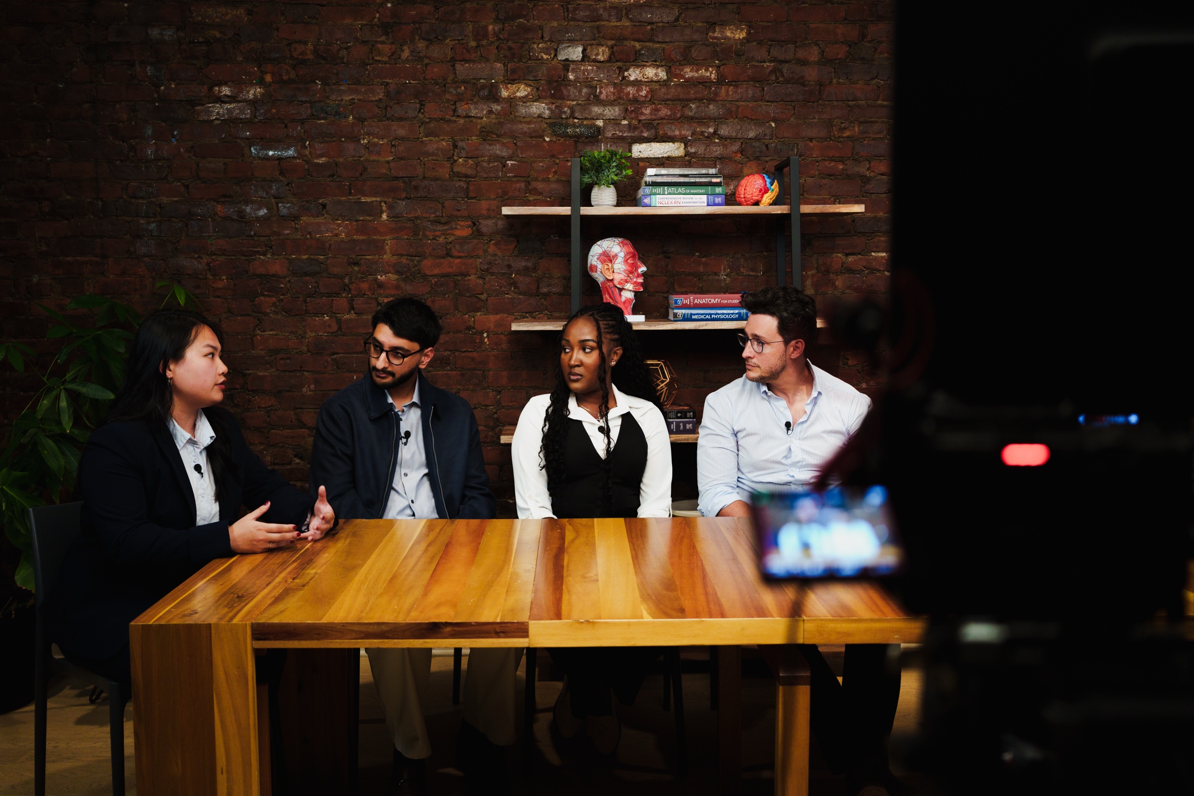 Four guests seated at the table mid conversation, a camera screen glowing out of focus in front