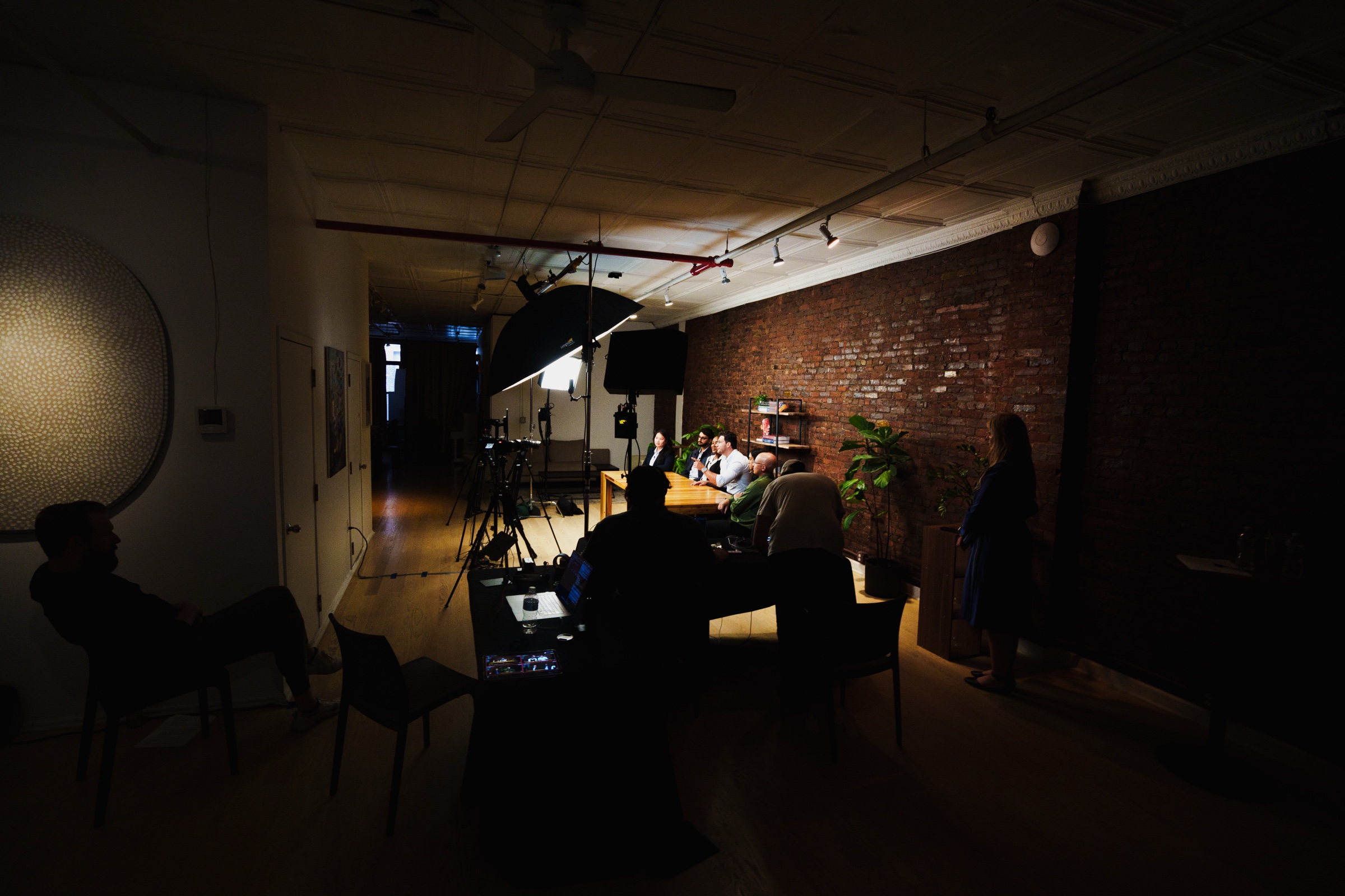 Wide dark room, a single pool of light on the table where the group records