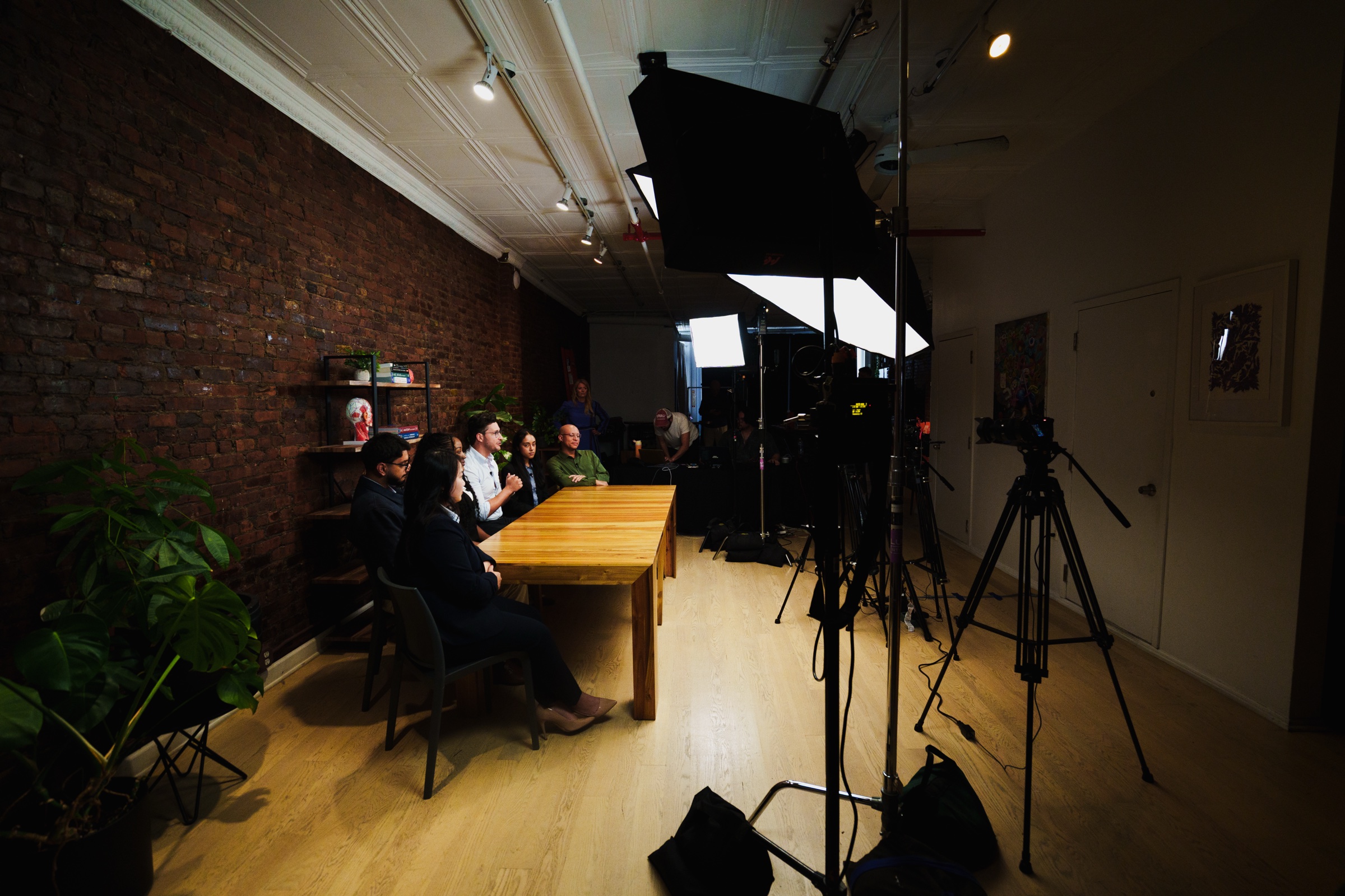 Side view down the brick wall showing the group at the table beyond lights and tripods