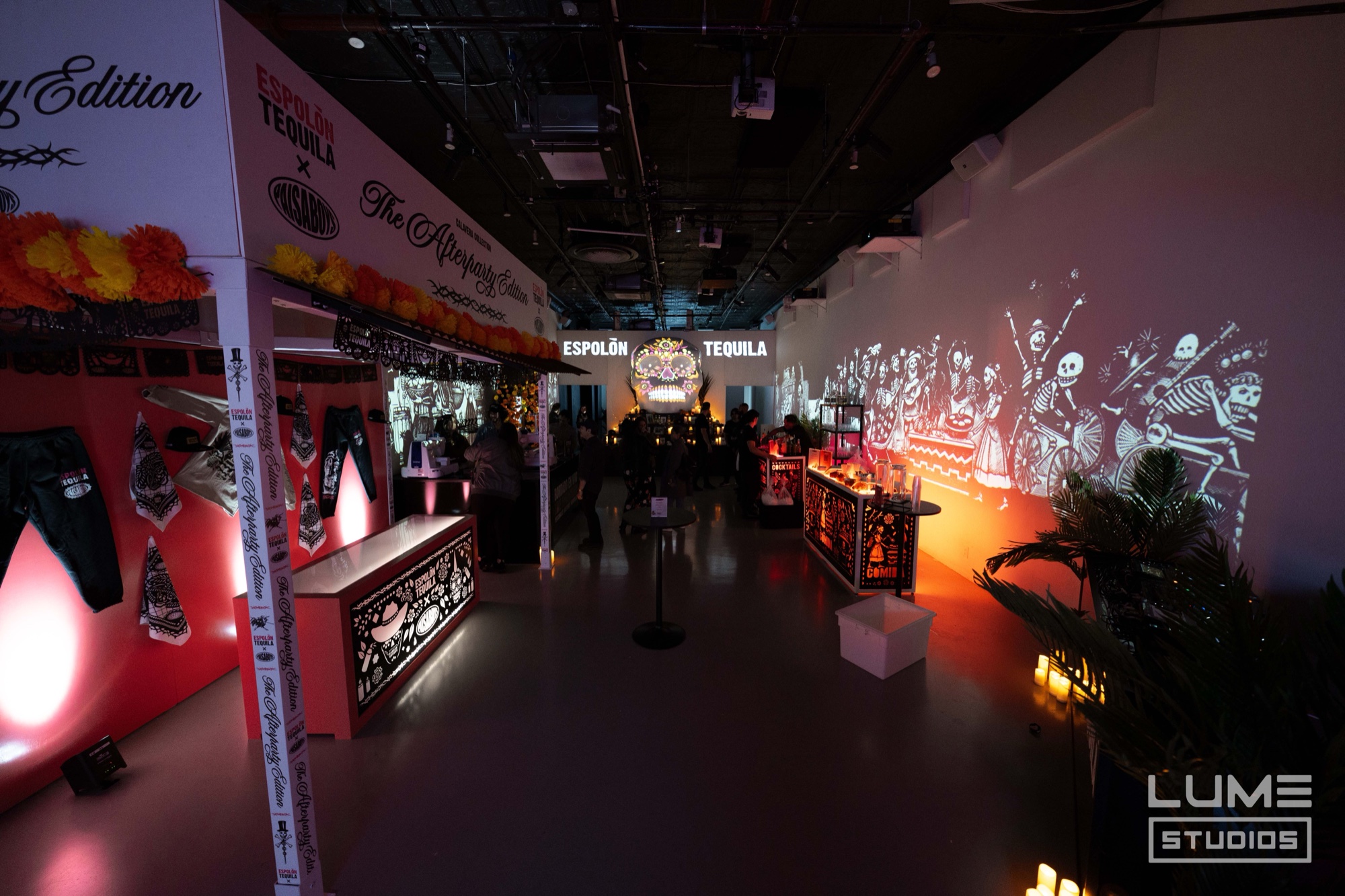 Dim event hall with Espolon Tequila signage, glowing red bars and skeleton figures projected on the far wall