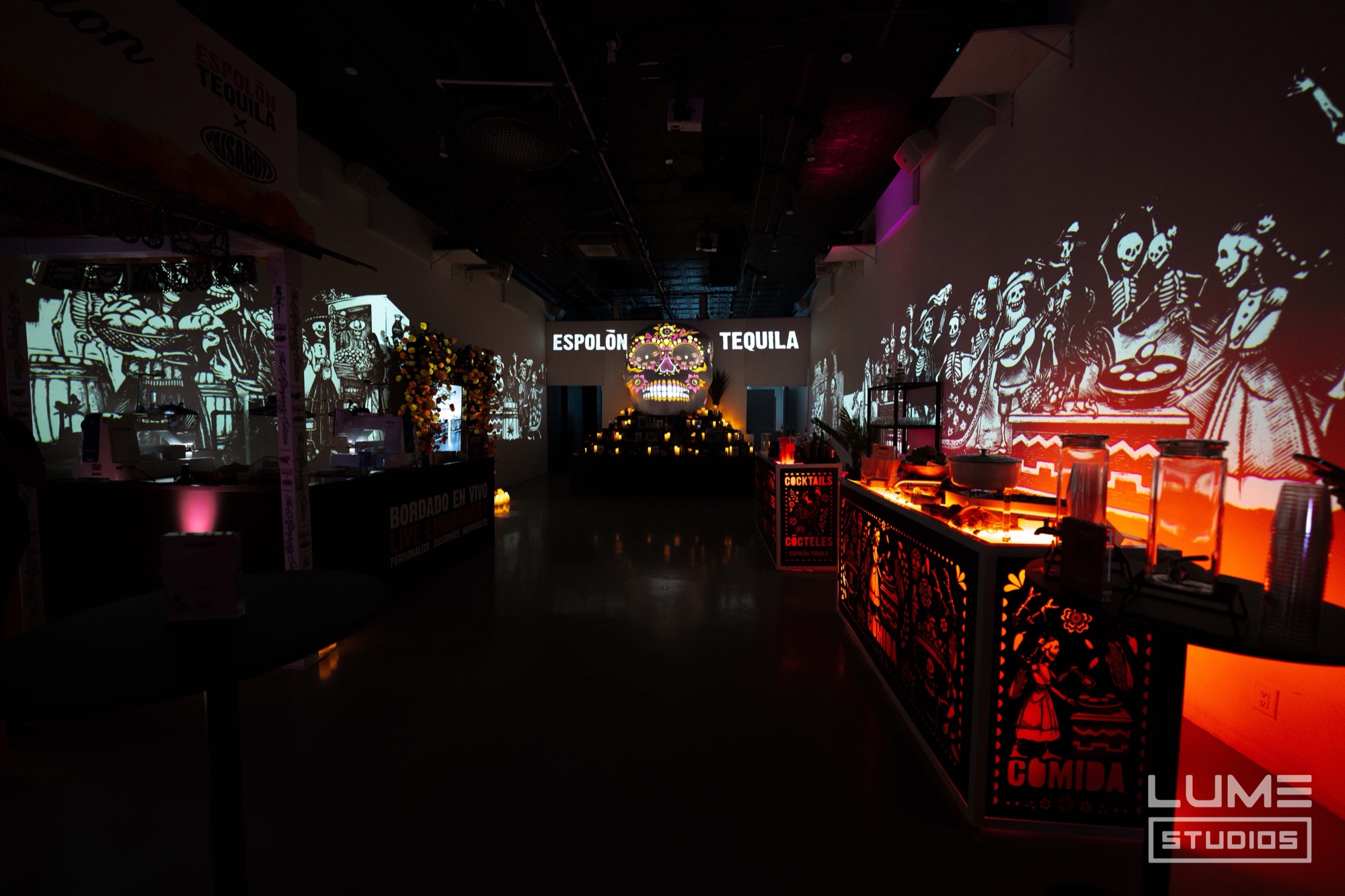 Dark hall lit by orange bars and skeleton wall projections leading to an Espolon Tequila altar