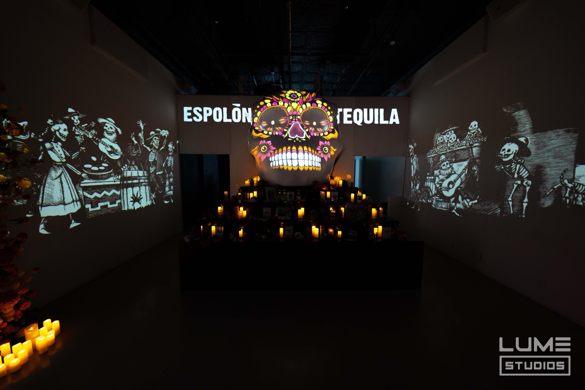 Projected sugar skull glowing between the words Espolon Tequila above tiers of candles and dancing skeletons