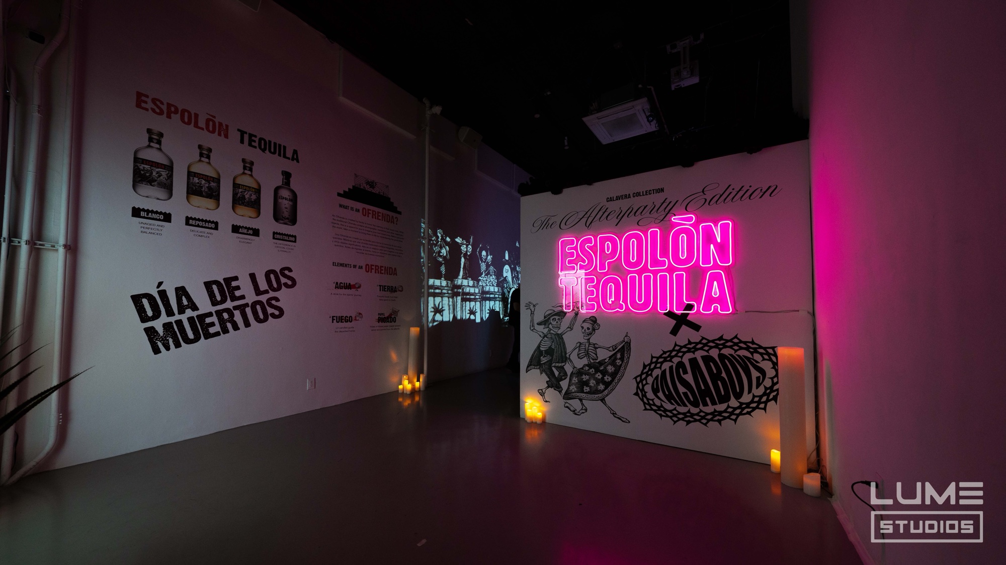 Pink neon Espolon Tequila sign beside a Dia de los Muertos wall with bottle illustrations and skeleton drawings