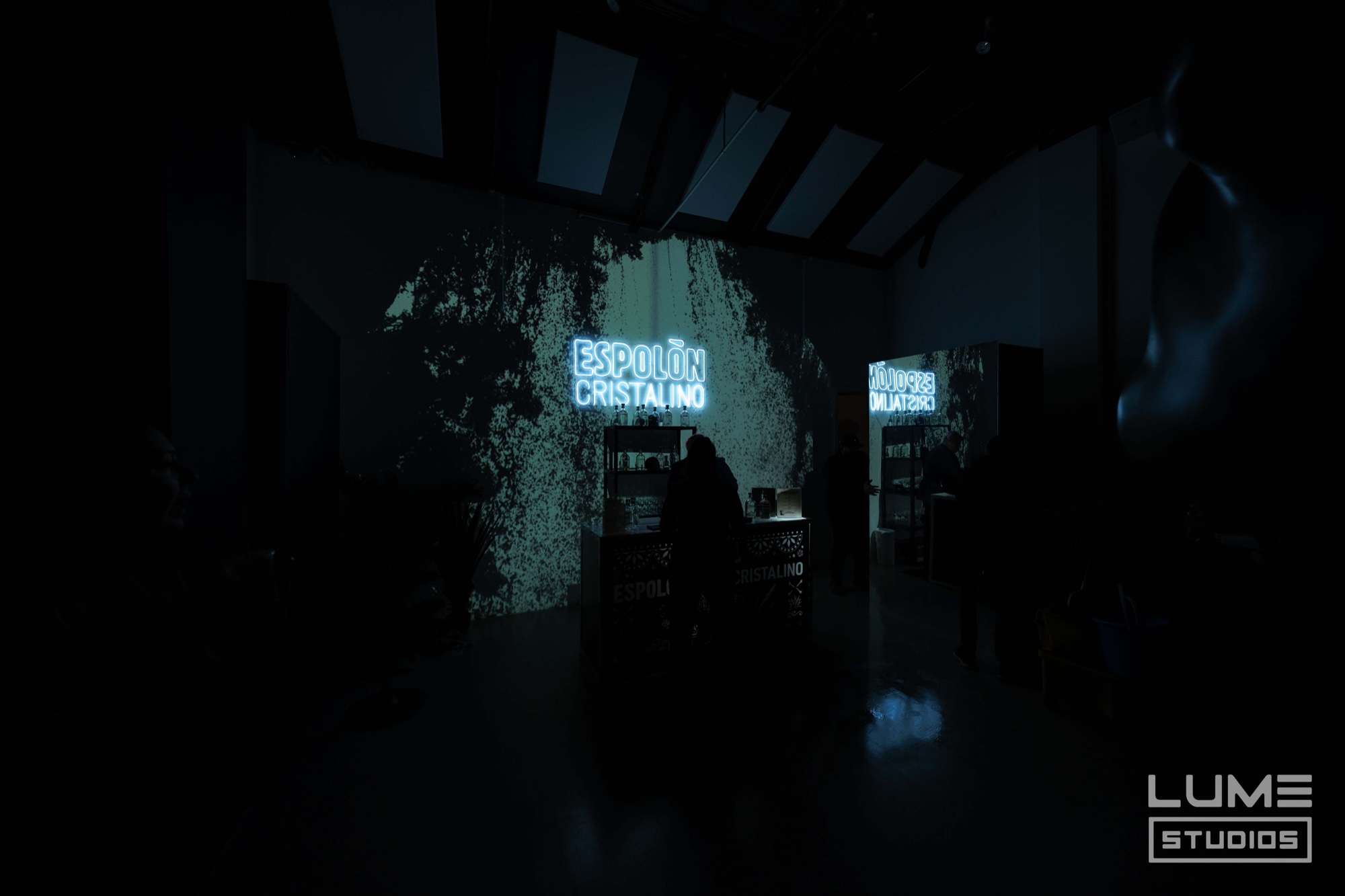 Near dark room with a glowing Espolon Cristalino sign and a mottled blue projection over a bar