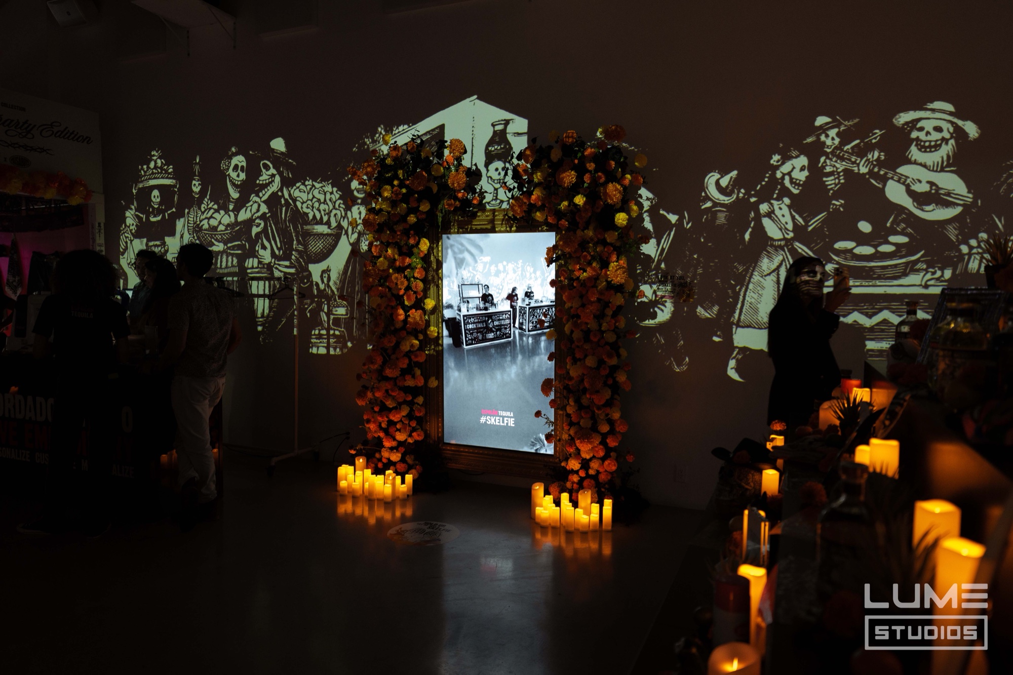 Screen framed by an arch of orange marigolds and candles with skeleton figures projected on surrounding walls