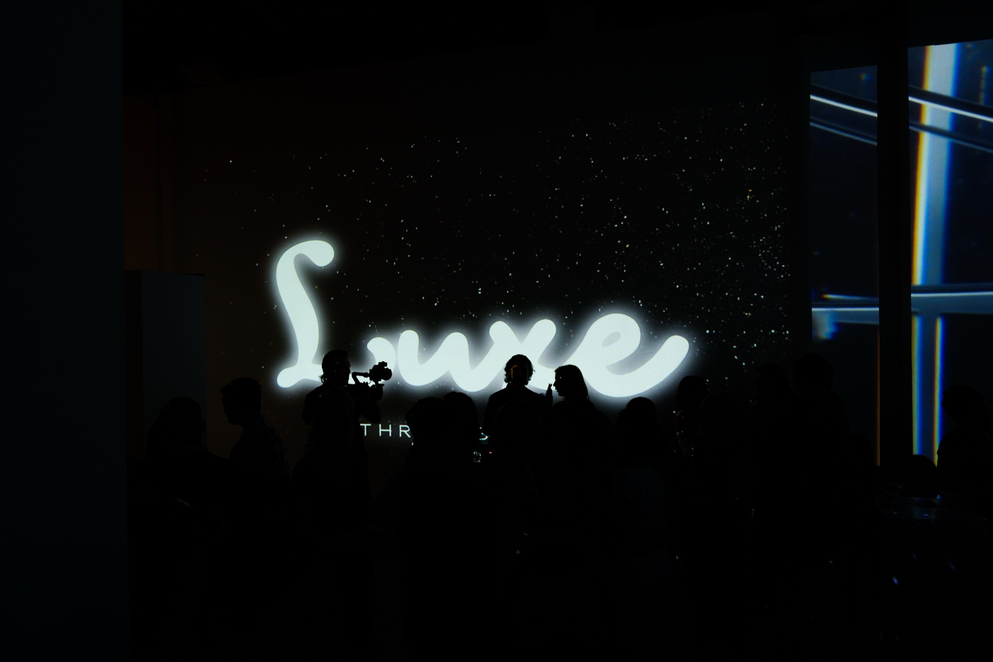 Silhouetted guests in front of the word Luxe glowing in white script on a dark starry wall