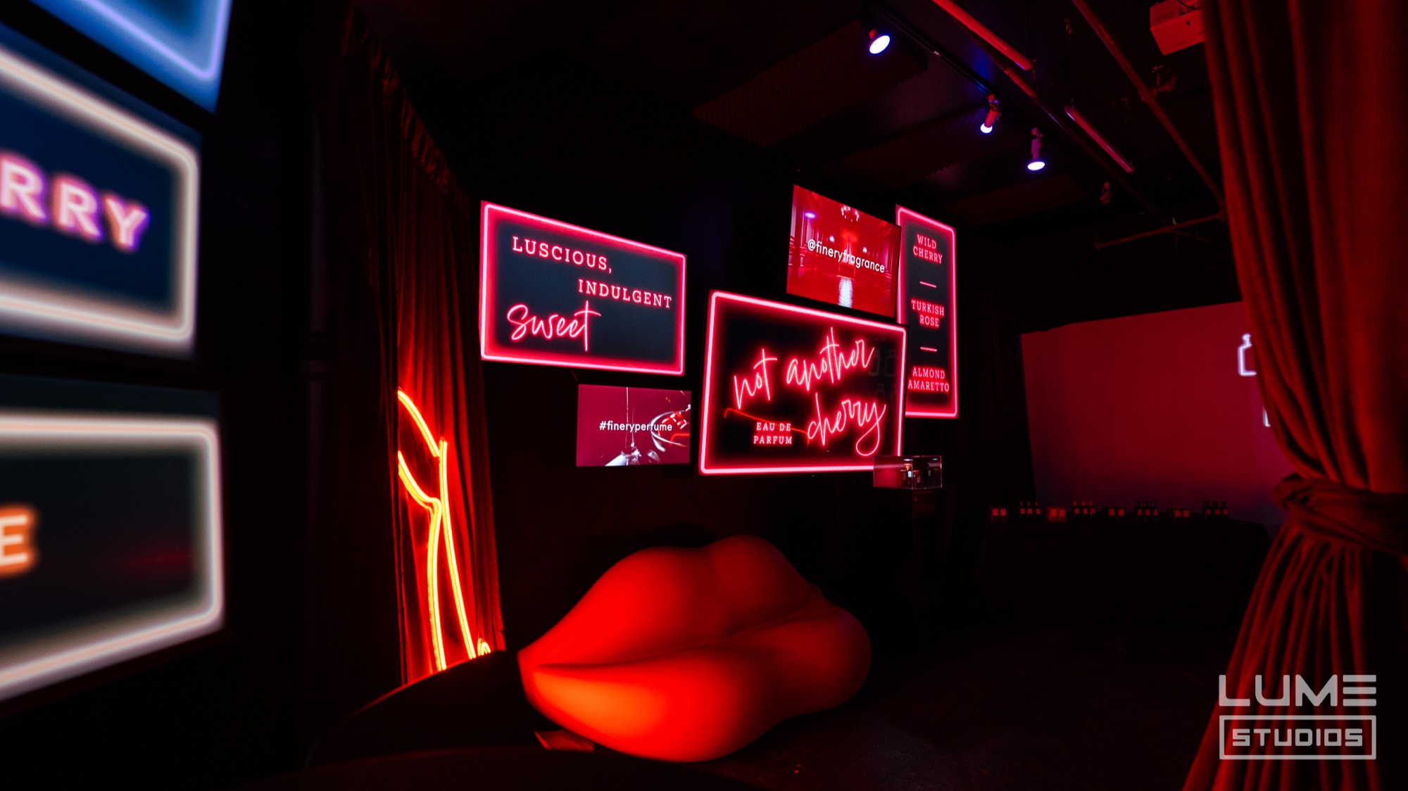 Red neon signs reading Luscious Indulgent Sweet and Not Another Cherry hang above a red lips sofa