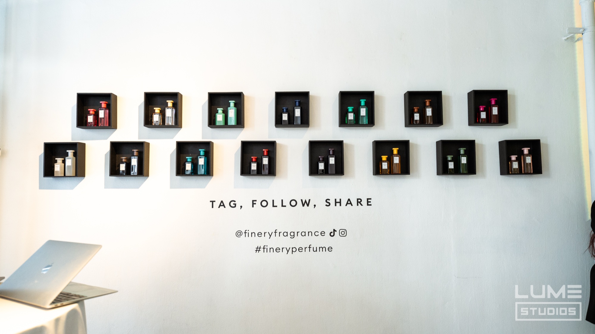 White wall of black shadow boxes holding perfume bottles above the words tag, follow, share and Finery handles