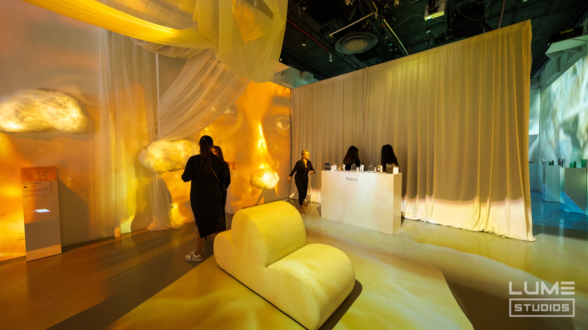 Yellow lit room draped in sheer white fabric with a glowing cloud shape, a curved white sofa and a counter