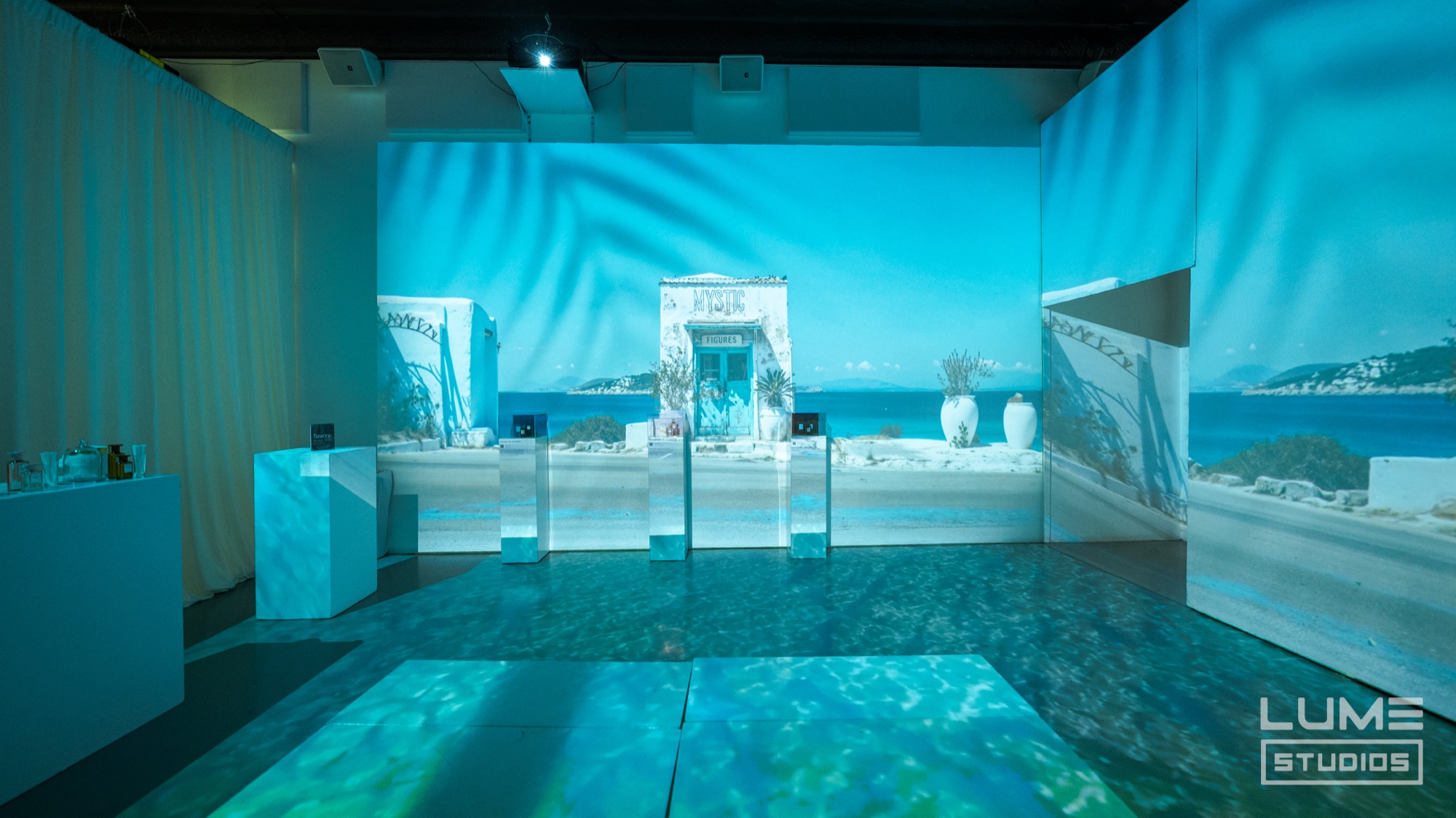 White display plinths on a rippling water floor inside a room projected with a Greek island seascape