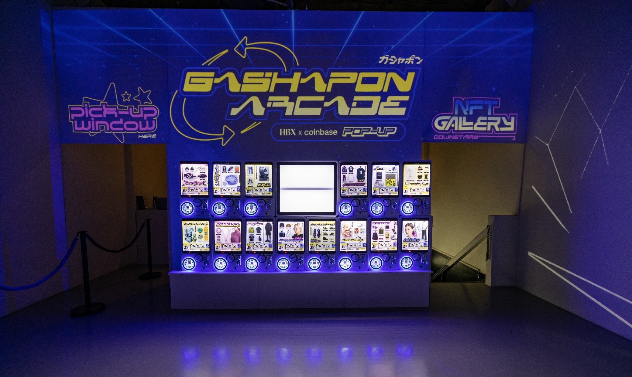 Rows of illuminated gashapon machines beneath neon HBX x Coinbase projection graphics