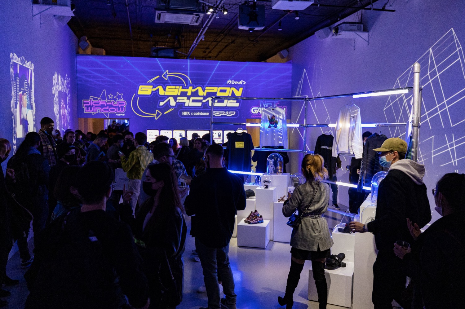 Crowd mingles among glowing merch racks and pedestals at the Hypebeast x Coinbase arcade