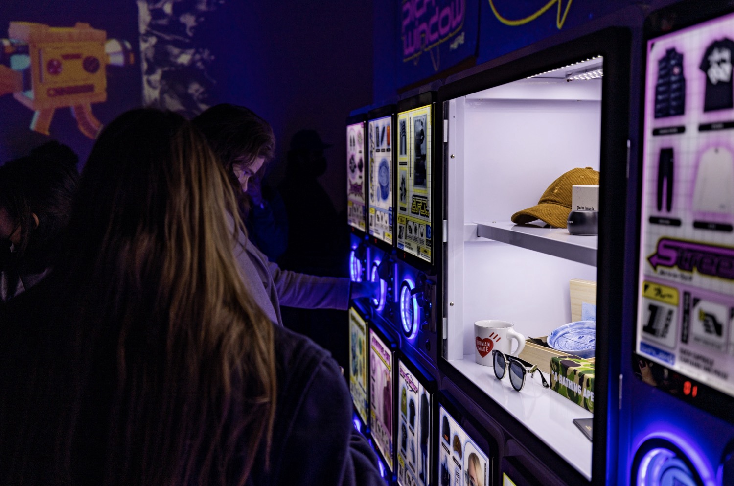 Visitor turns a capsule machine crank near a prize window stocked with streetwear goods