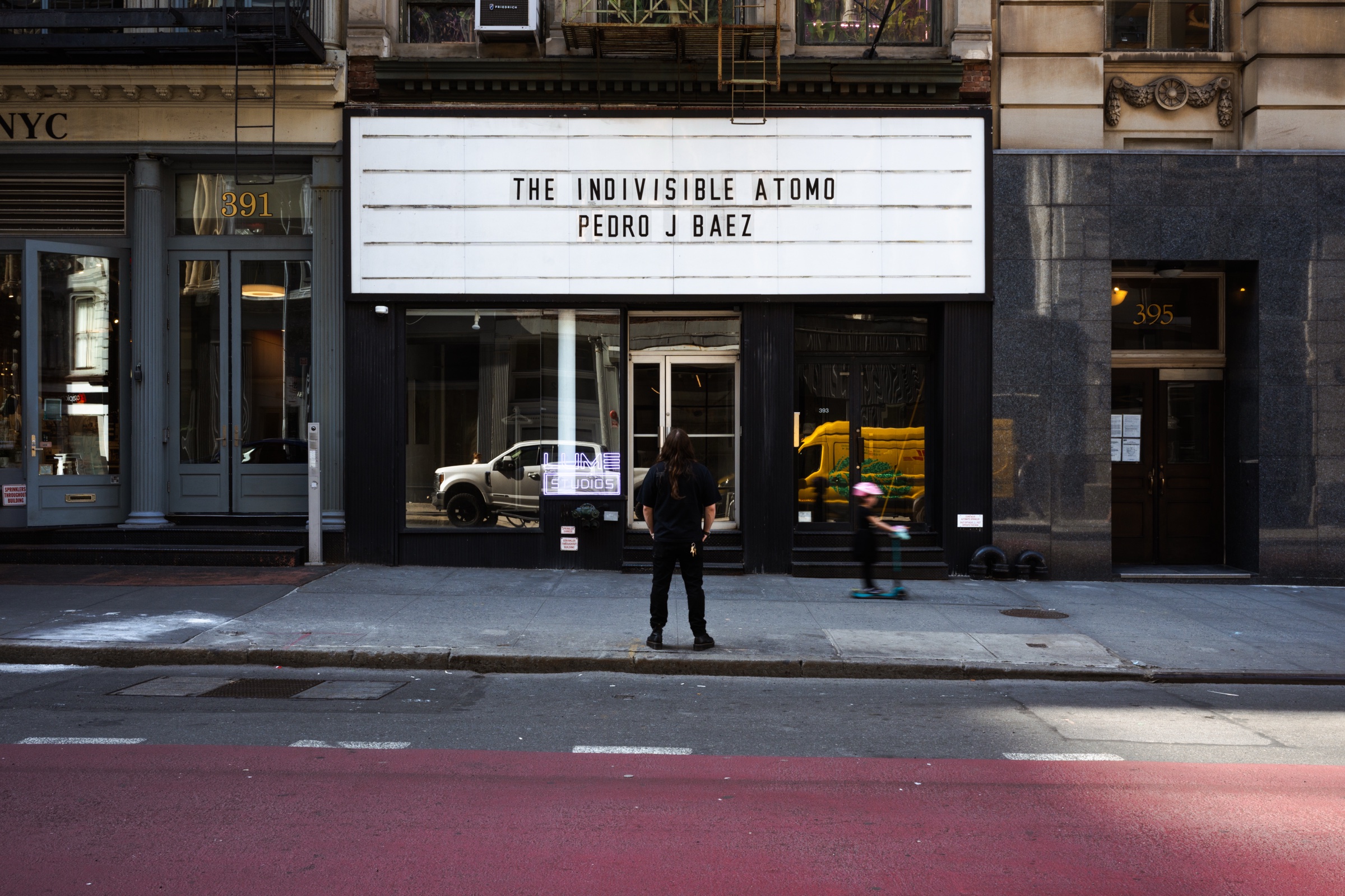 Black gallery marquee on a Manhattan street reading THE INDIVISIBLE ATOMO PEDRO J BAEZ above the entrance