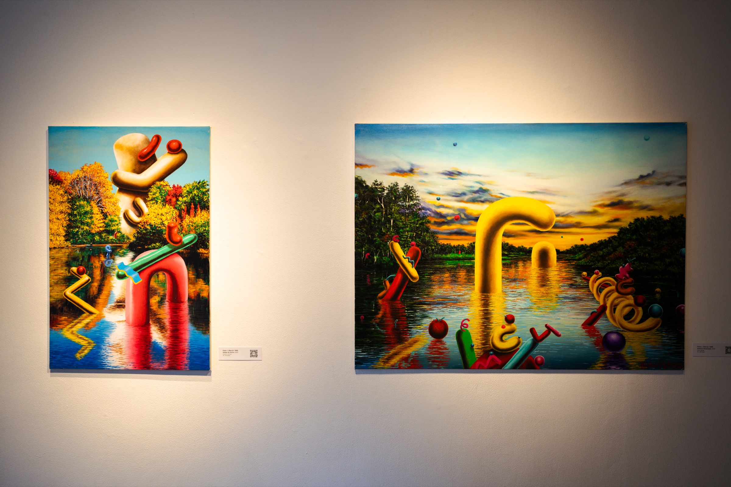 Two landscape paintings with yellow tubular forms over water hang side by side on a pale wall