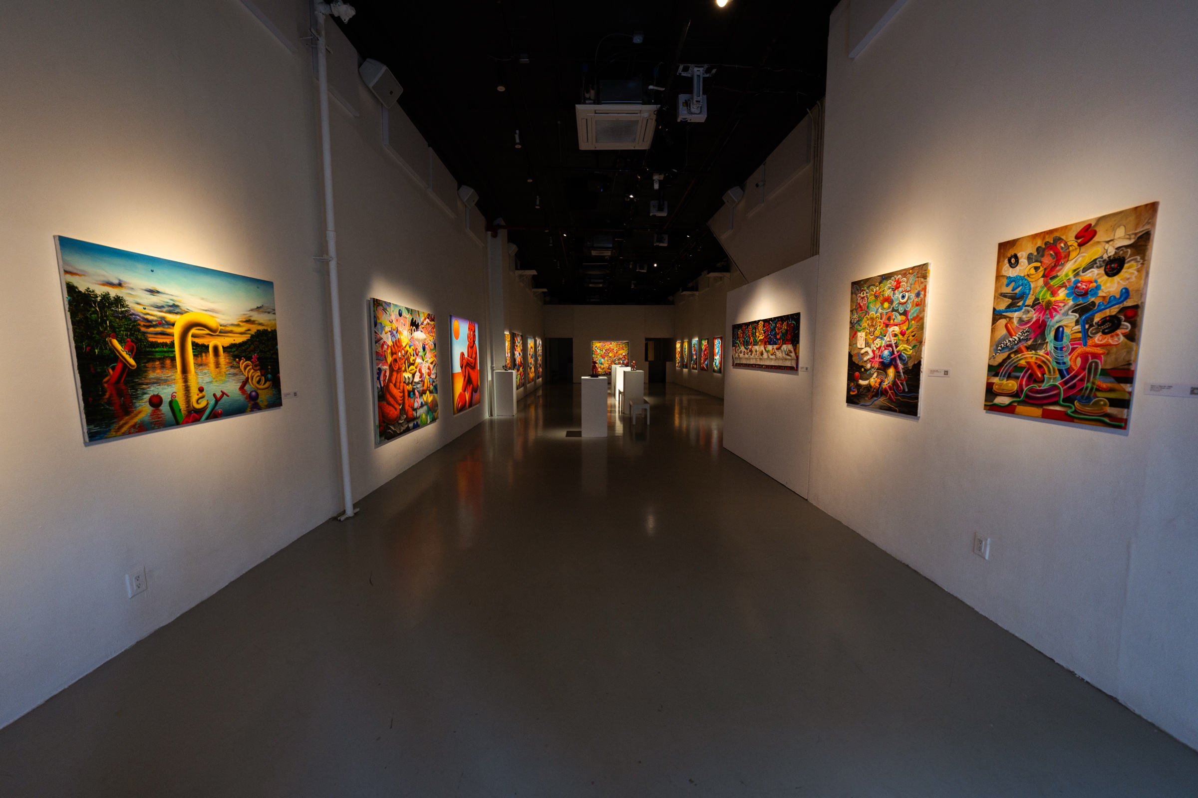 Long corridor of white walls hung with cartoon paintings under a black ceiling, sculpture lit at the far end