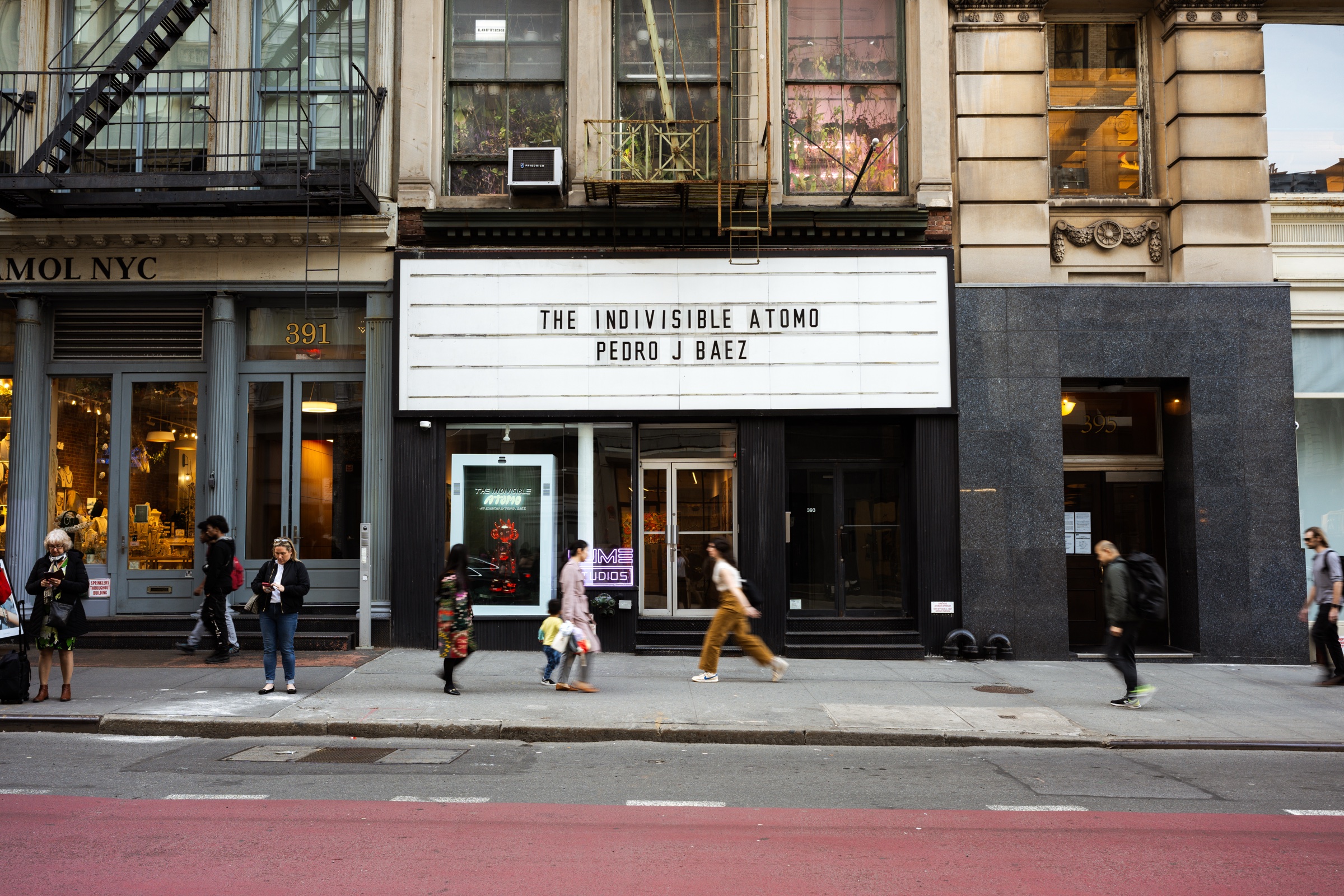 People walk past the gallery entrance beneath the marquee on a sunlit city sidewalk