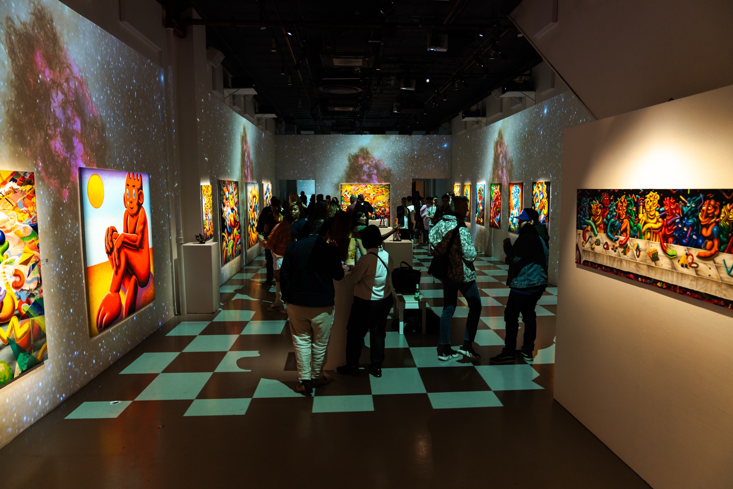 A crowd moves through a starlit projection room past glowing canvases and a checkered green floor