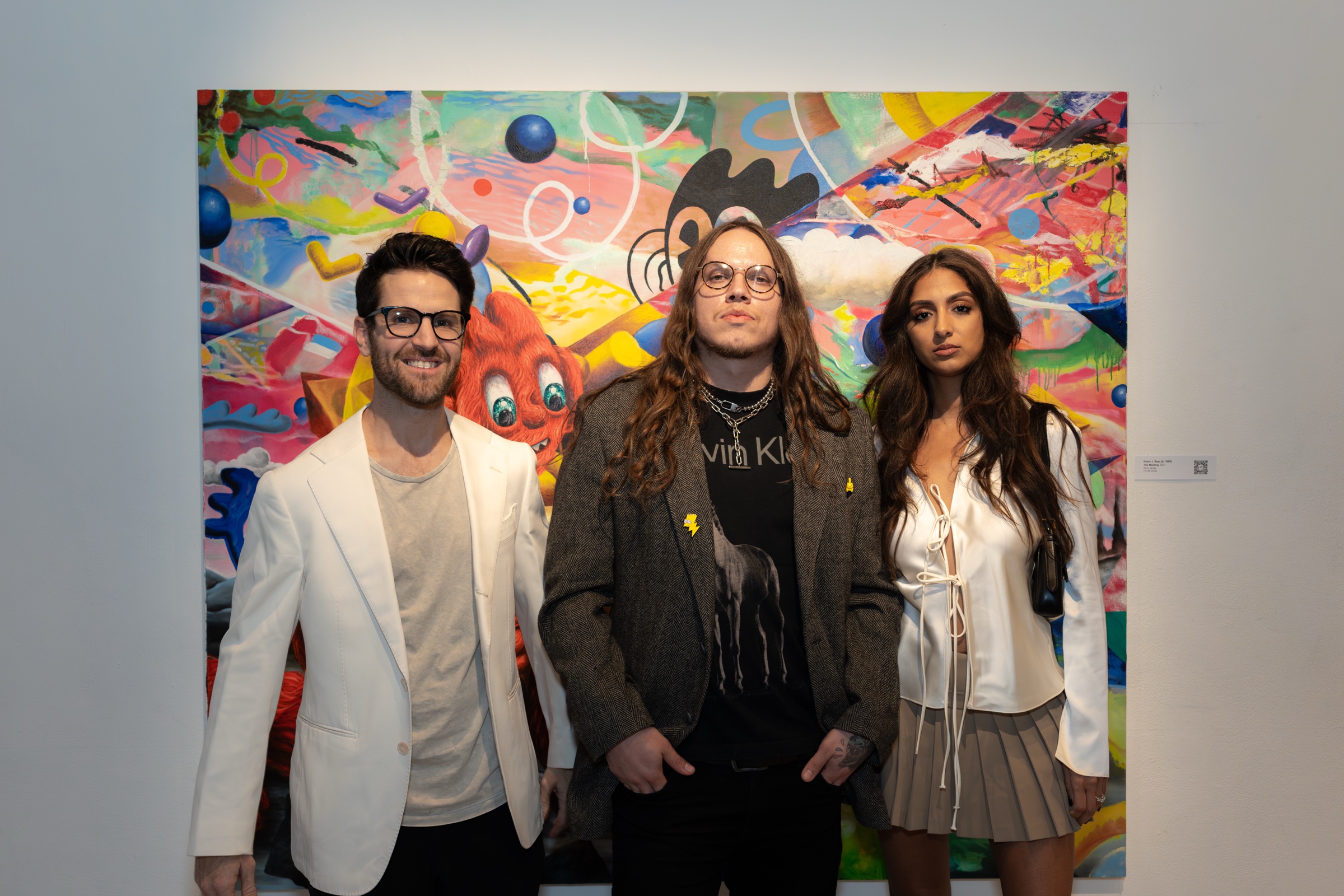 Three guests pose in front of a large painting of an orange creature among coloured shapes